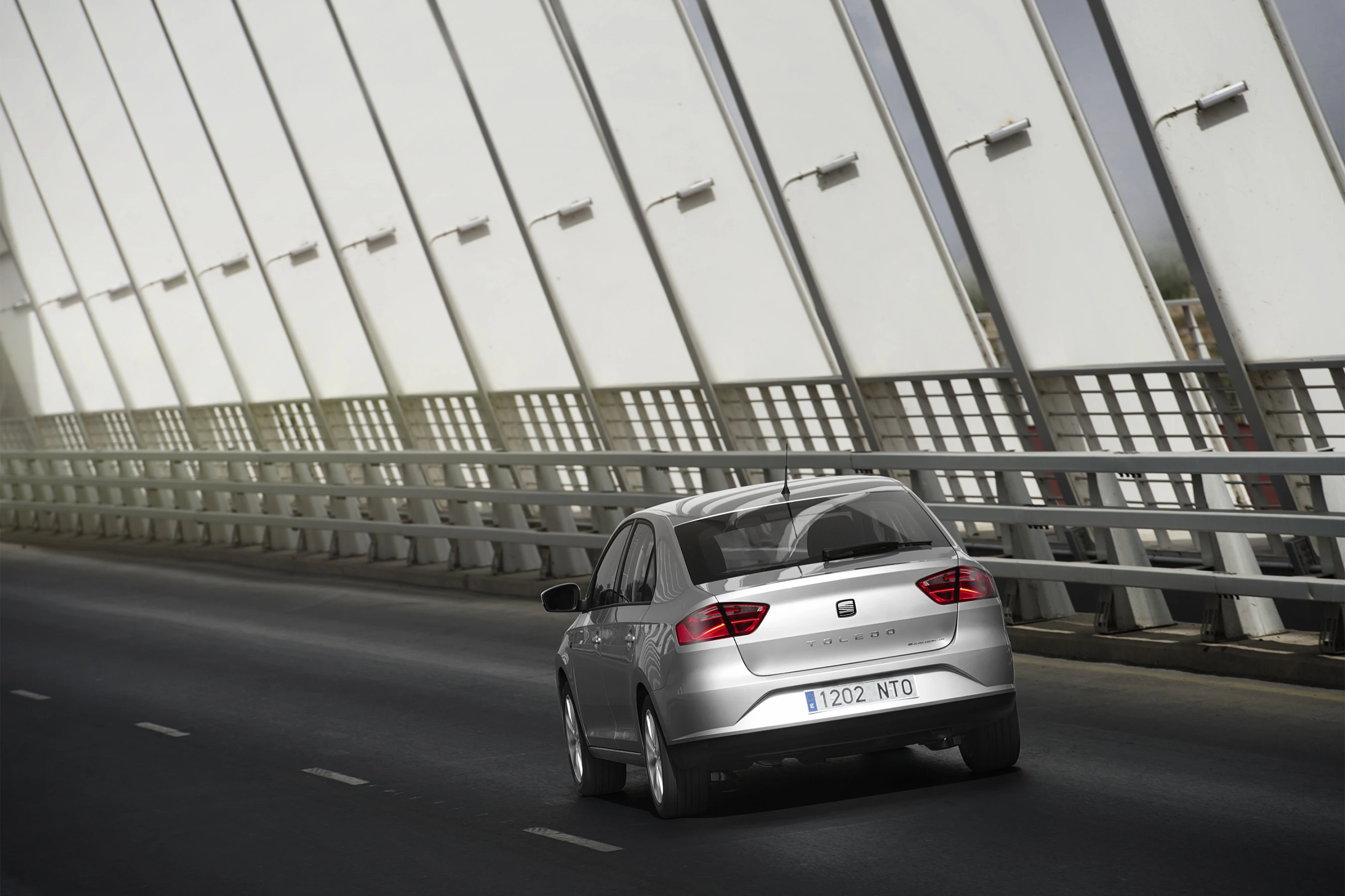Silbernes Auto fährt auf einer Brücke mit modernen, schrägen Streben und bewölktem Himmel im Hintergrund.