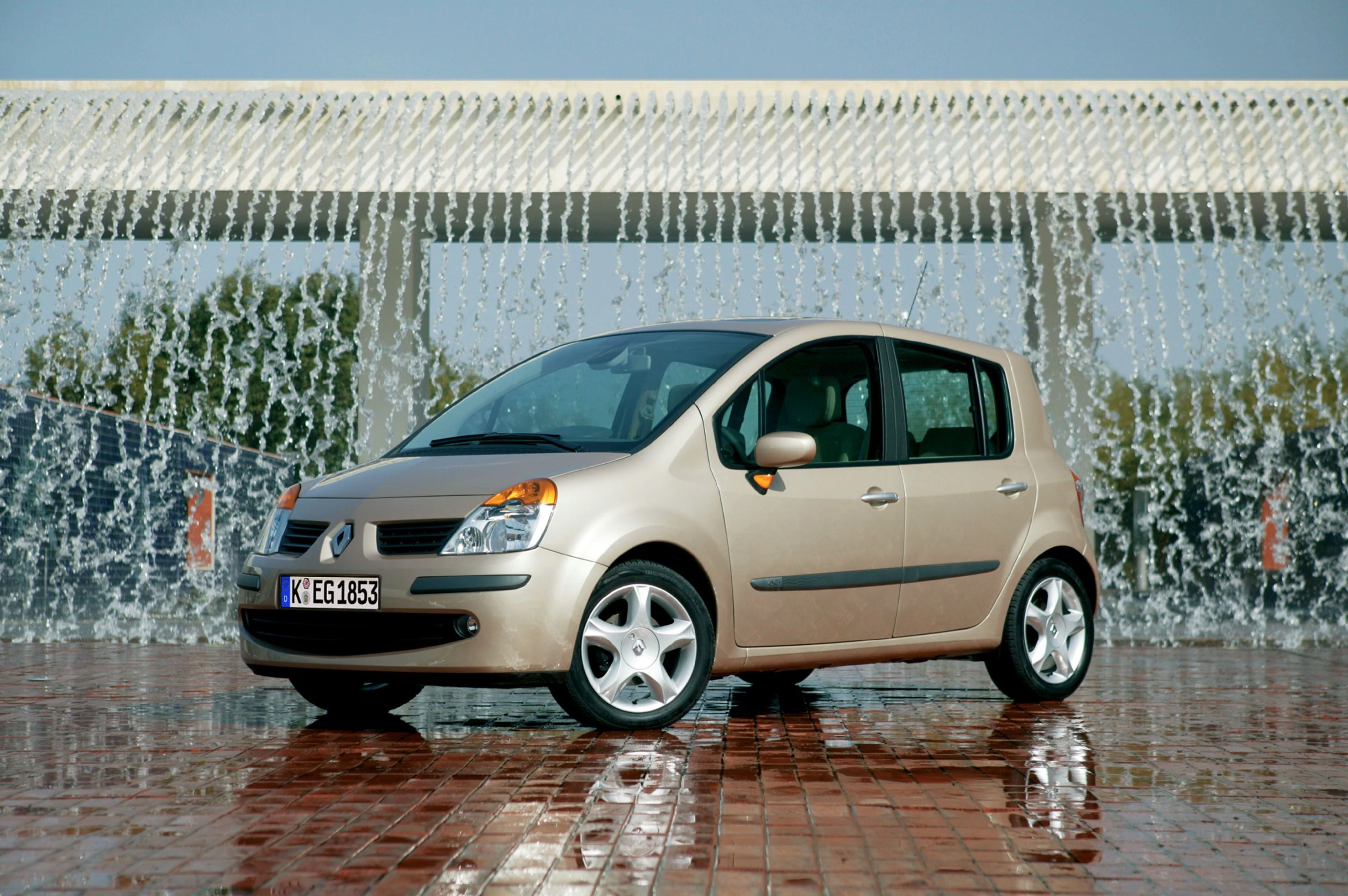 Beiger Renault Modus steht vor einem riesigen Wasserfall auf nassem Pflaster.