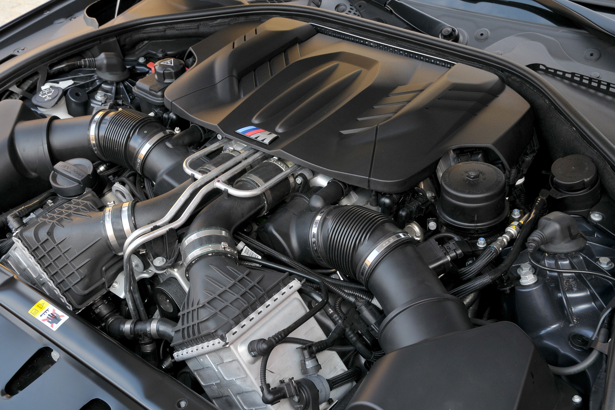 Nahaufnahme eines hochwertigen Automotors mit mehreren Rohren und Kabeln, sauber und gut organisiert in einem schwarzen Motorraum.