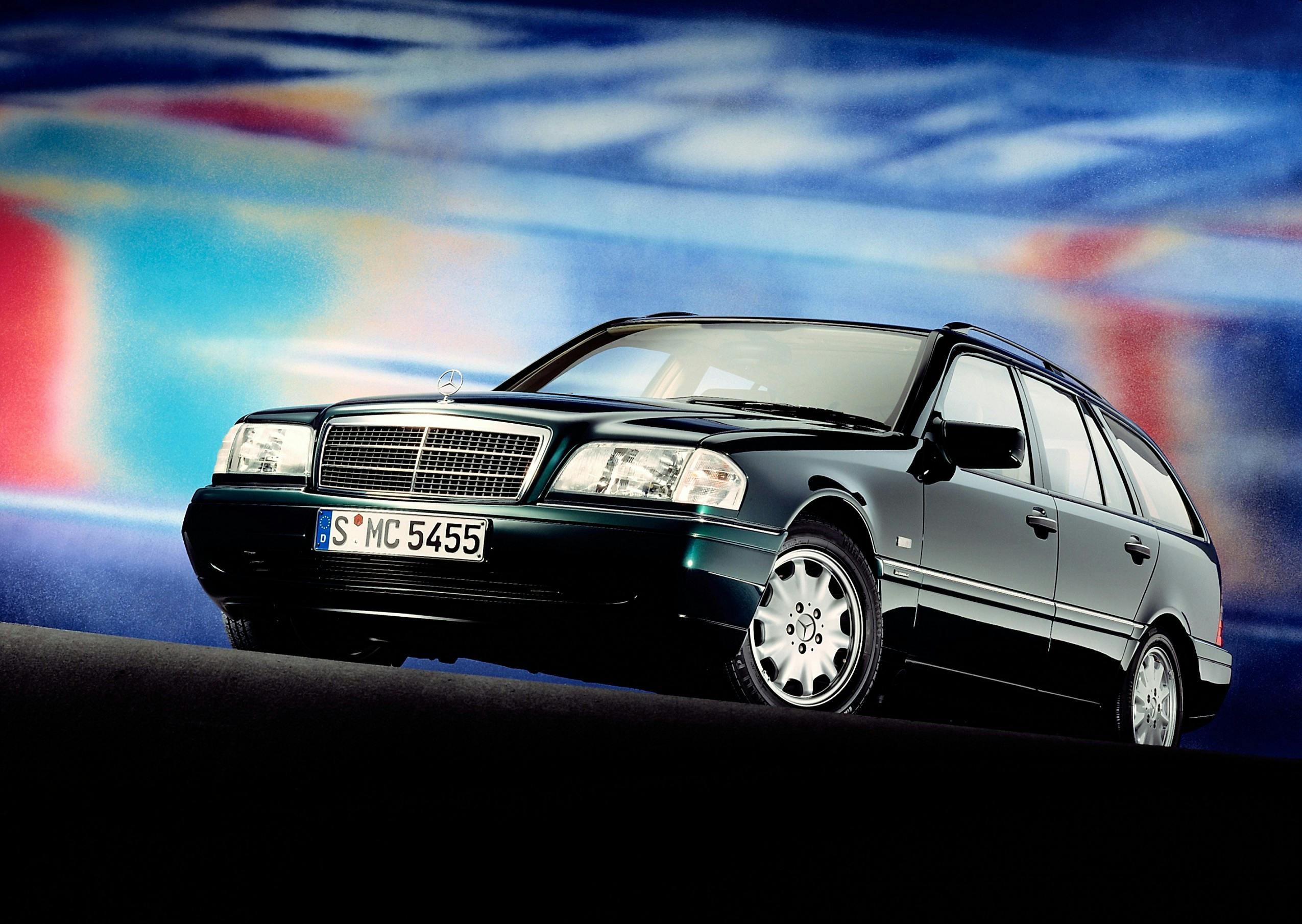 Schwarzer Kombi der 1990er Jahre vor einem farbenfrohen, verschwommenen Hintergrund. Frontansicht mit deutlichem Kühlergrill.