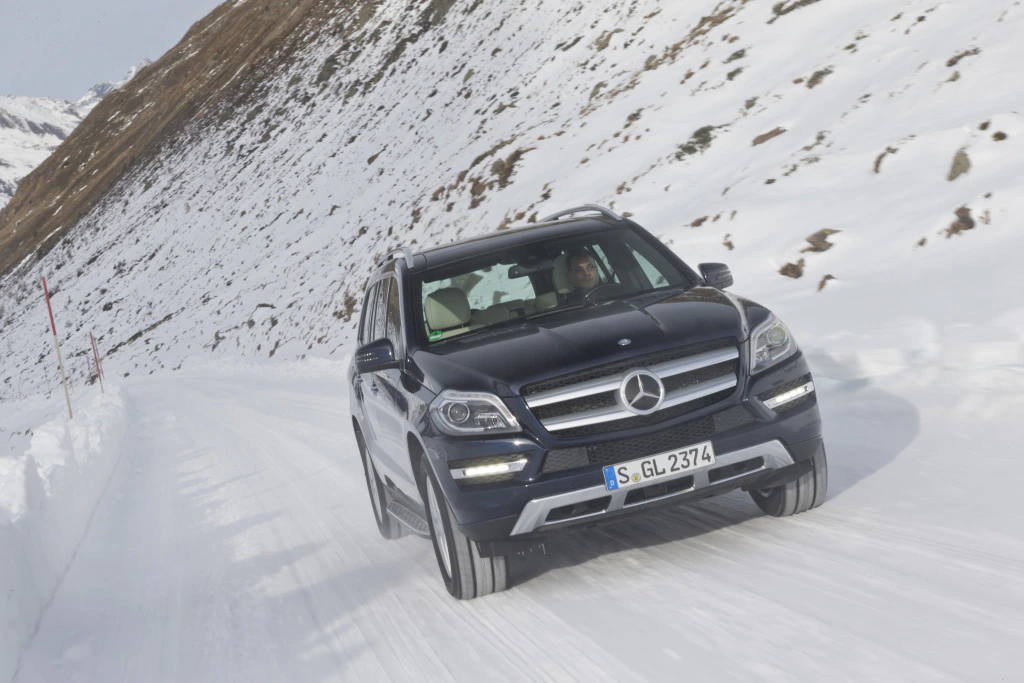 Ein schwarzer Mercedes-Benz SUV fährt auf einer schneebedeckten Straße durch eine winterliche Berglandschaft.