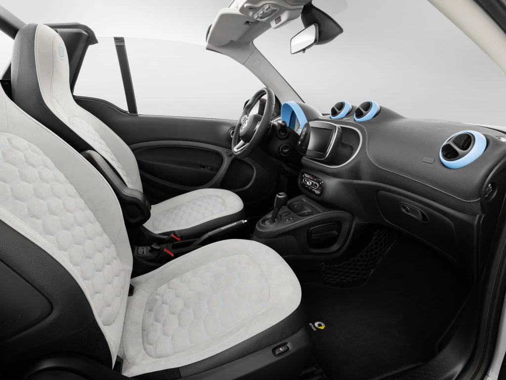Innenraum eines modernen Autos mit weißen und schwarzen Sitzen, blauen Lüftungselementen und einem minimalistischen Armaturenbrettdesign.