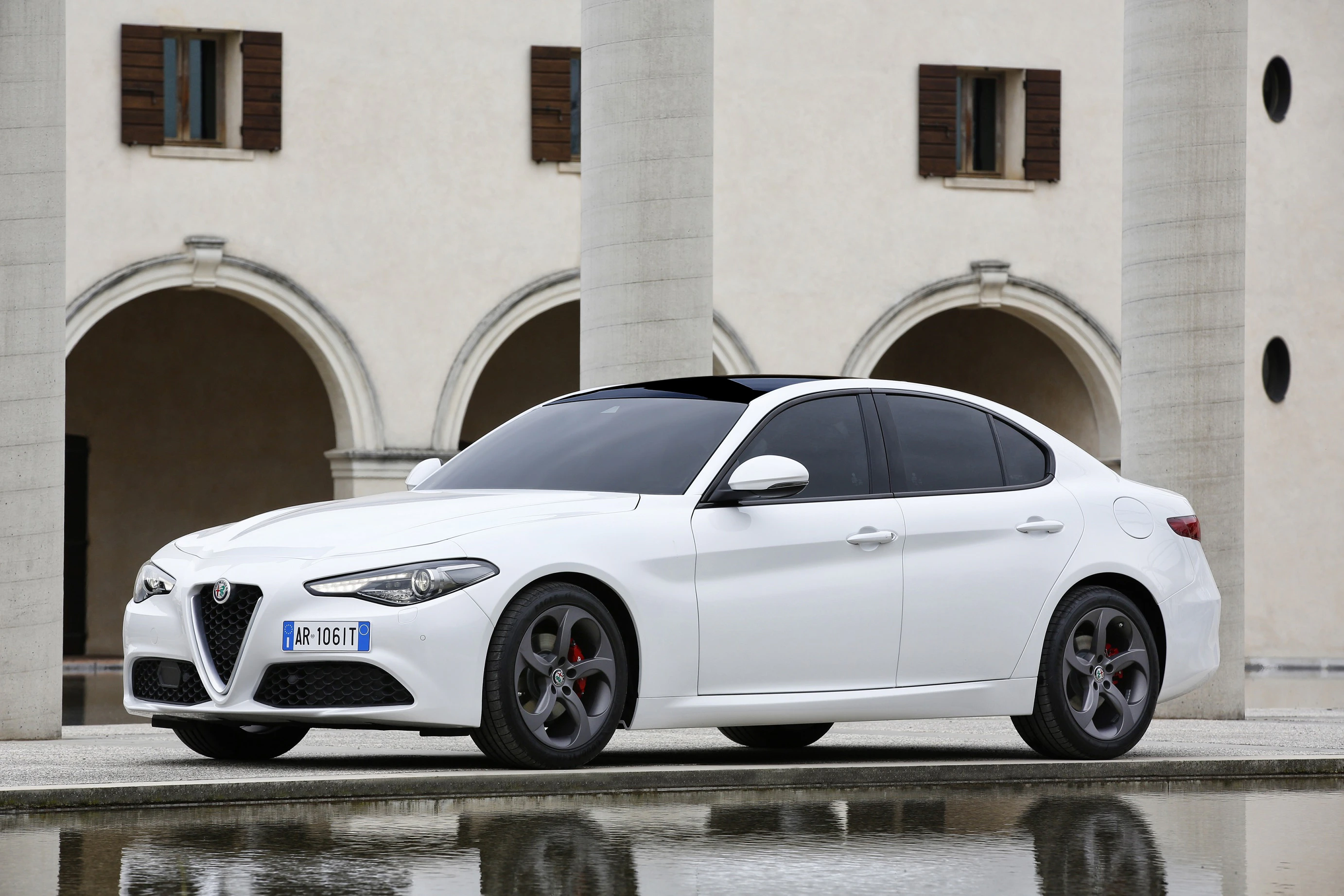 Weißer Alfa Romeo Giulia, geparkt vor einem Gebäude mit Rundbögen und Säulen, seitliche Ansicht.