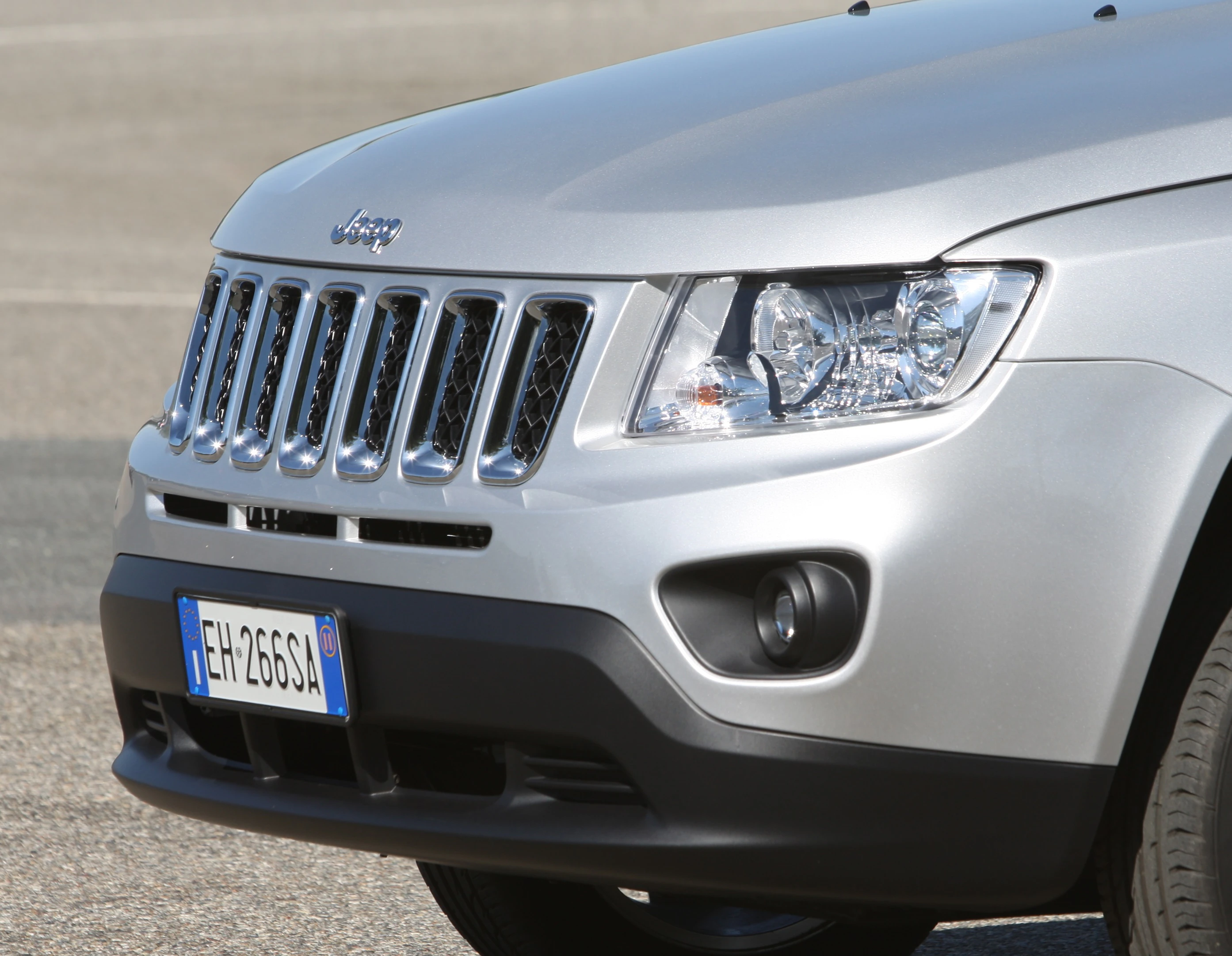 Silberner Jeep mit italienischem Kennzeichen, Frontansicht, betont Kühlergrill und Scheinwerfer, geparkt auf Asphalt.