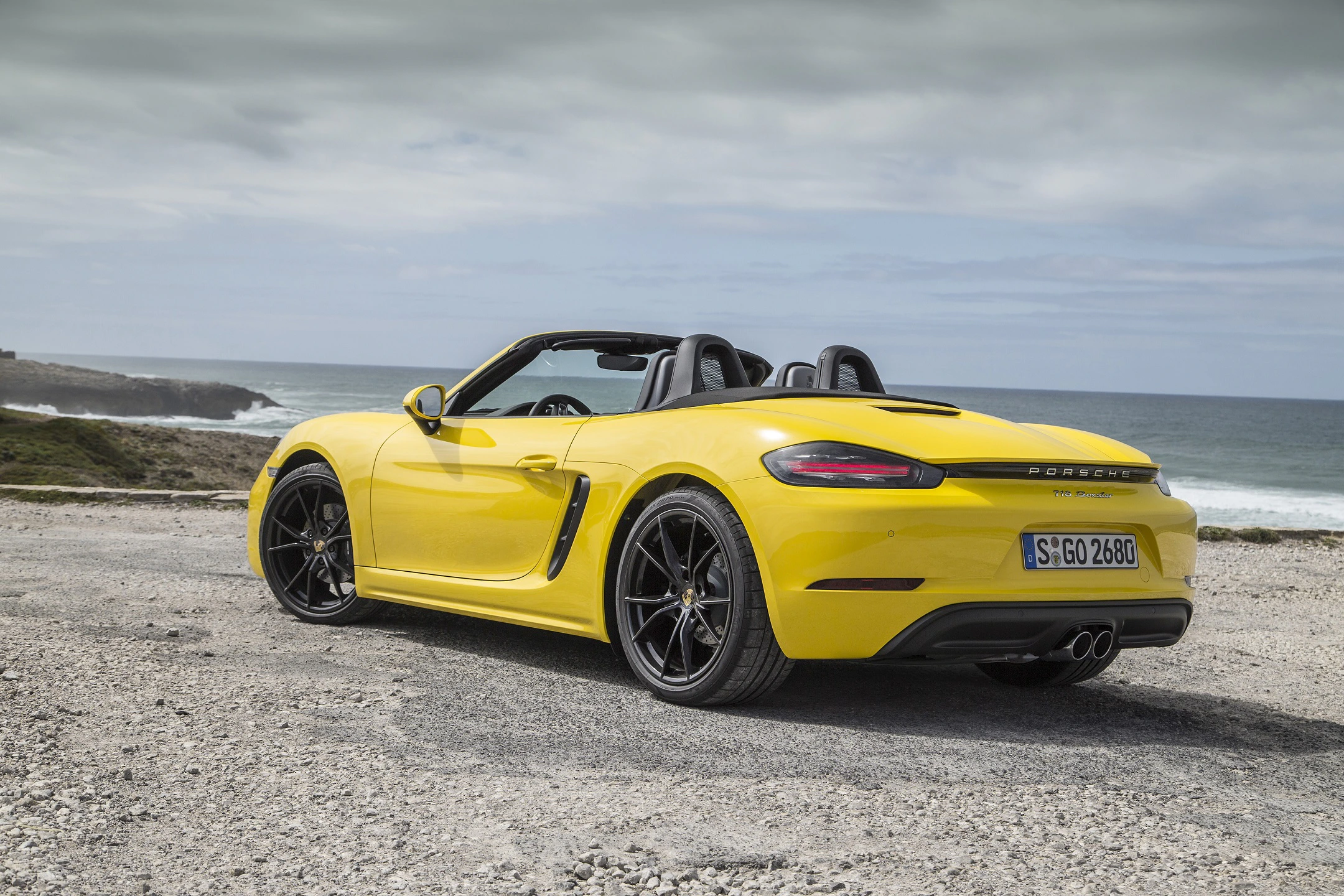 Gelber Sportwagen-Cabrio parkt auf einer Küstenstraße mit Blick aufs Meer unter bewölktem Himmel.