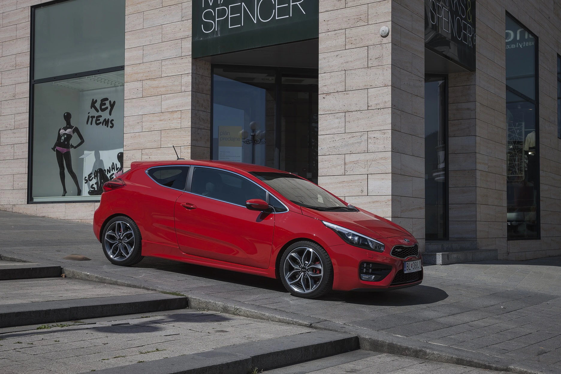 Rotes Auto parkt neben einem modernen Gebäude mit Schaufenstern, auf denen "Key Items" steht. Steckstufen im Vordergrund.