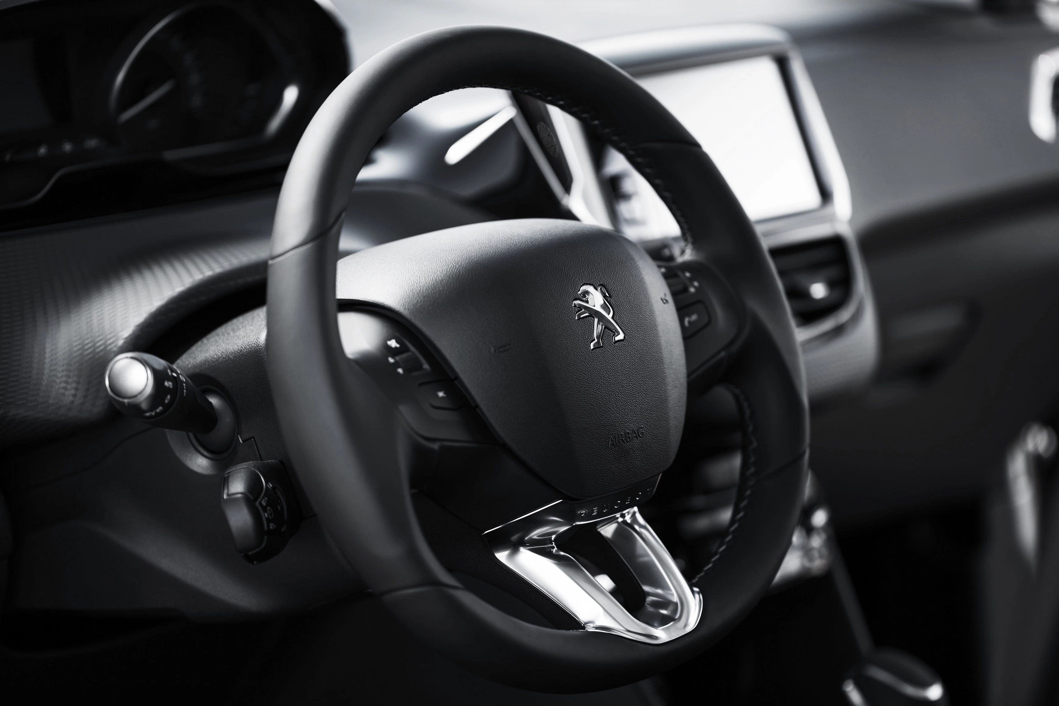Nahaufnahme eines Lenkrads mit dem Peugeot-Logo in einem modernen Auto, umgeben von Instrumententafel und Bedienelementen.