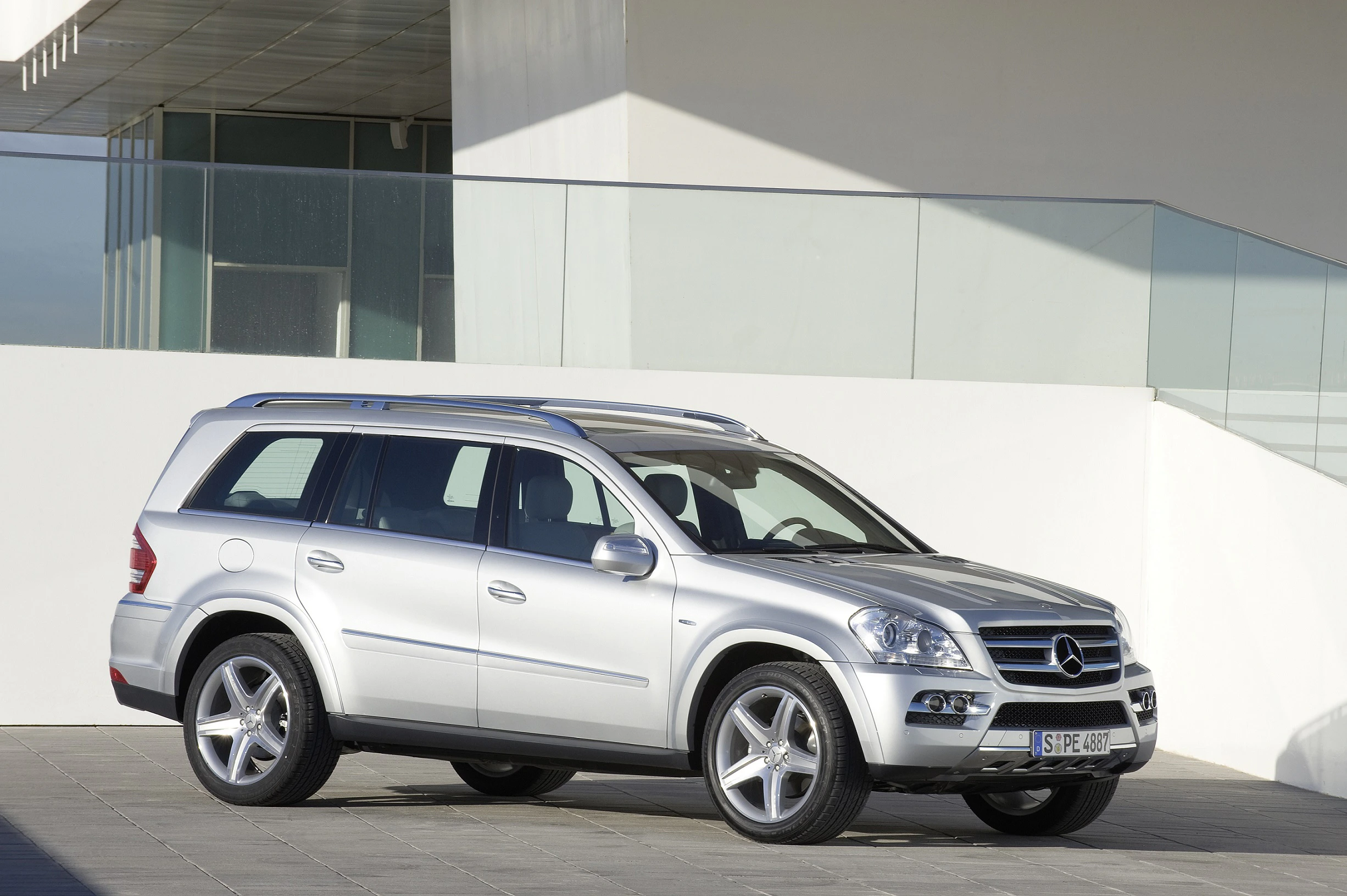 Silberner SUV, geparkt auf einem modernen, hellen Platz vor einem Gebäude mit Glas- und Betonarchitektur.