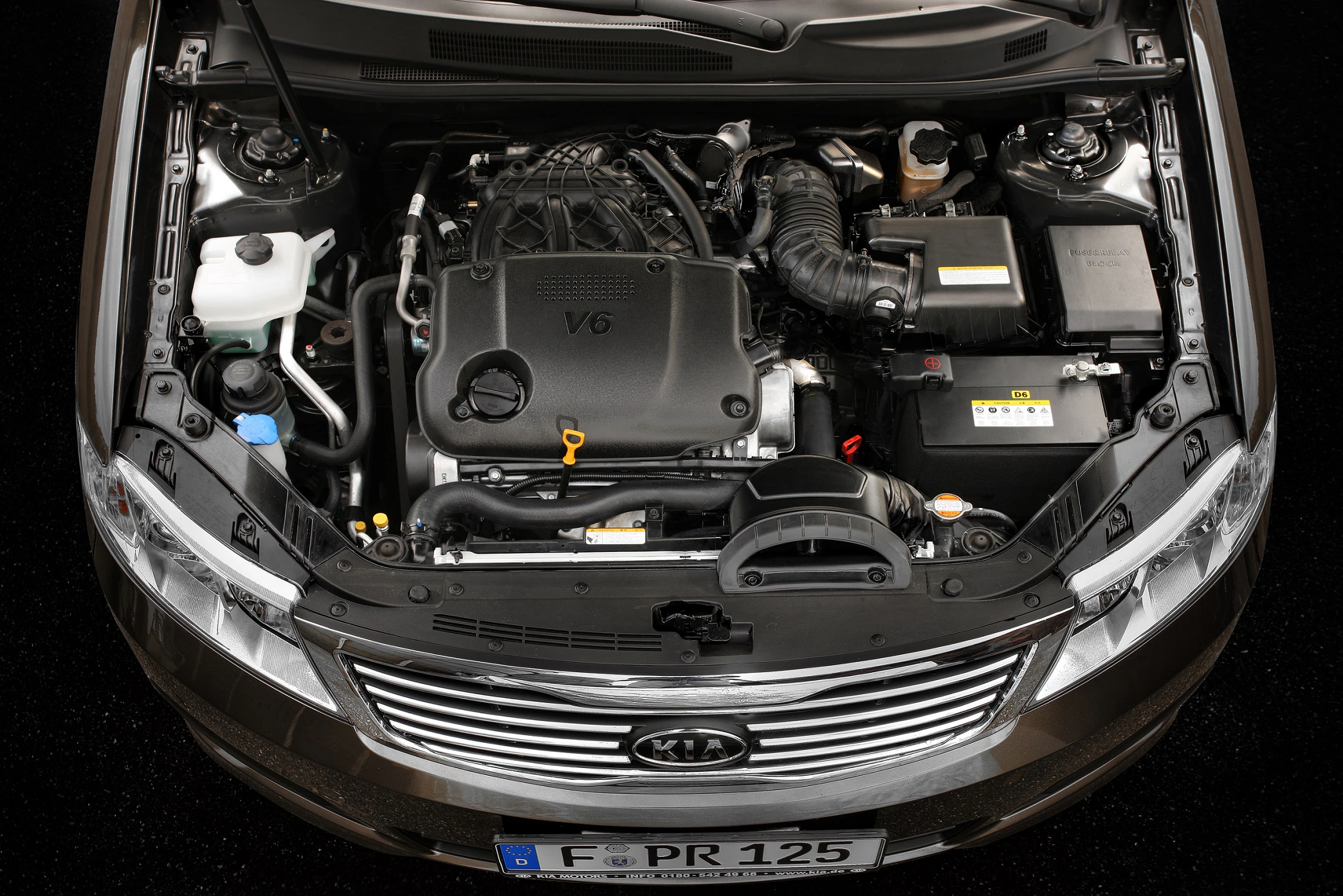 Motorraum eines Kia mit V6-Motor, sichtbarer Kühlergrill und deutschen Kennzeichen.
