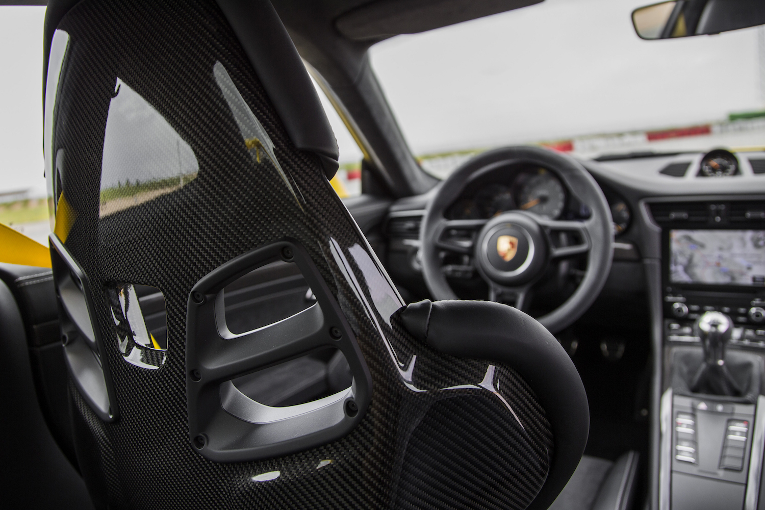 Sicht von der Rückbank eines Autos mit kohlefaserverstärktem Sitz und Cockpit-Ansicht, inklusive Lenkrad und Tachometer.