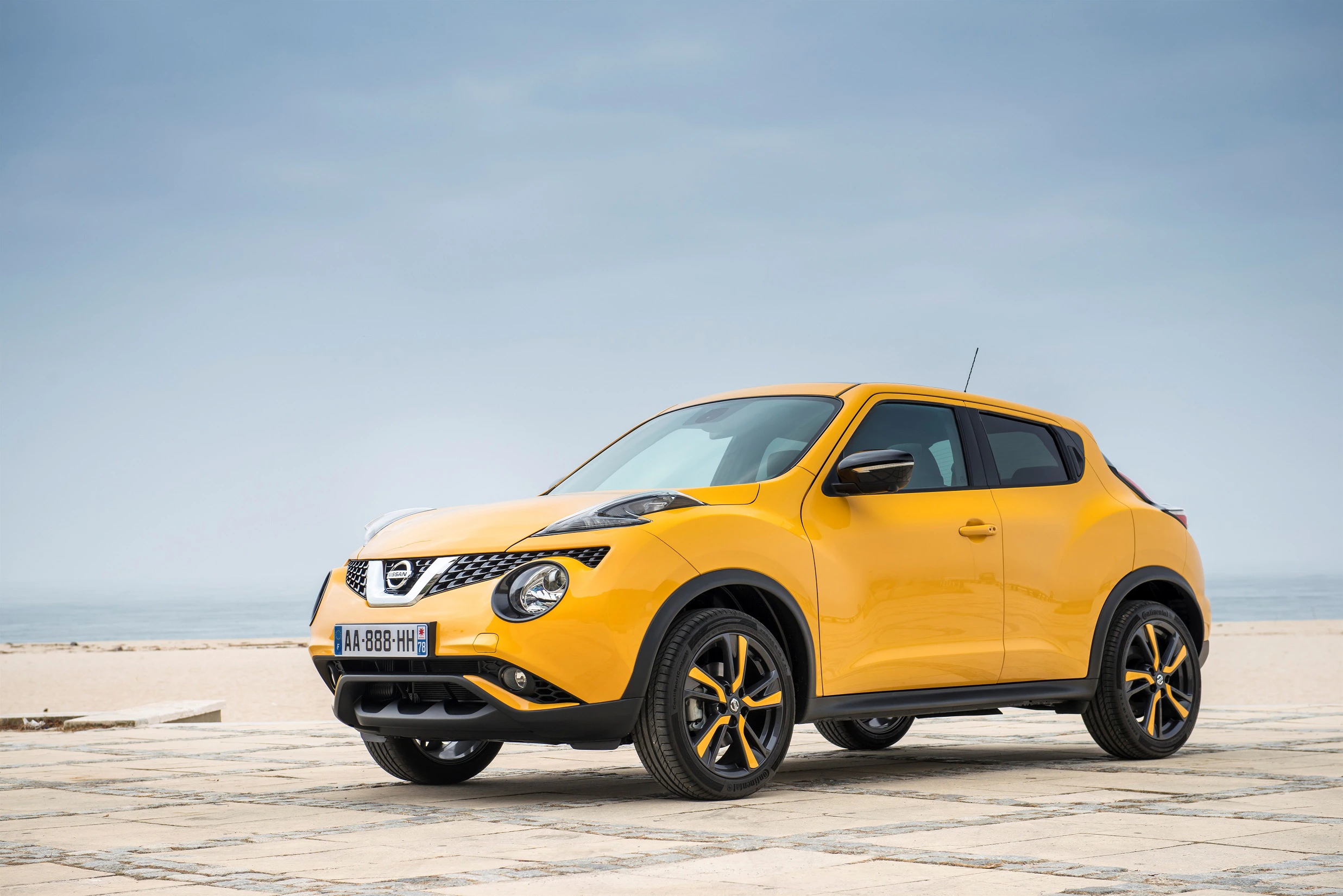Gelber Nissan Juke auf einem Parkplatz am Strand, bewölkter Himmel im Hintergrund.