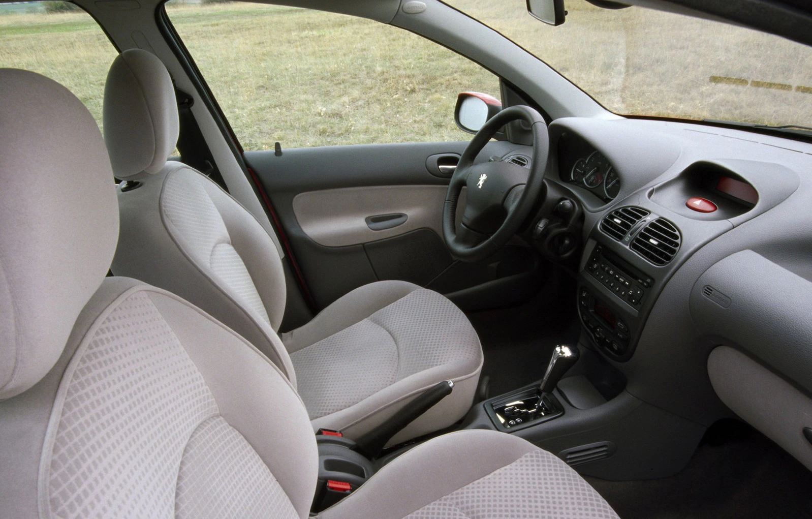 Innenraum eines Autos mit grauen Textilsitzen, Armaturenbrett mit Lenkrad und Schalthebel, Blick von der Rückbank nach vorne.