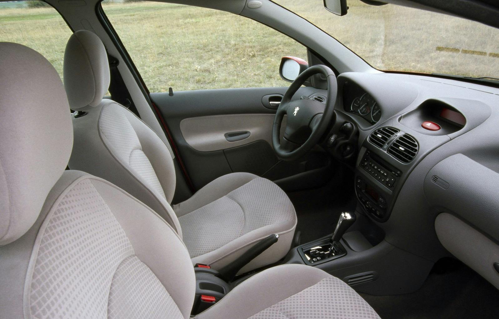 Innenraum eines Autos mit grauen Textilsitzen, Armaturenbrett mit Lenkrad und Schalthebel, Blick von der Rückbank nach vorne.