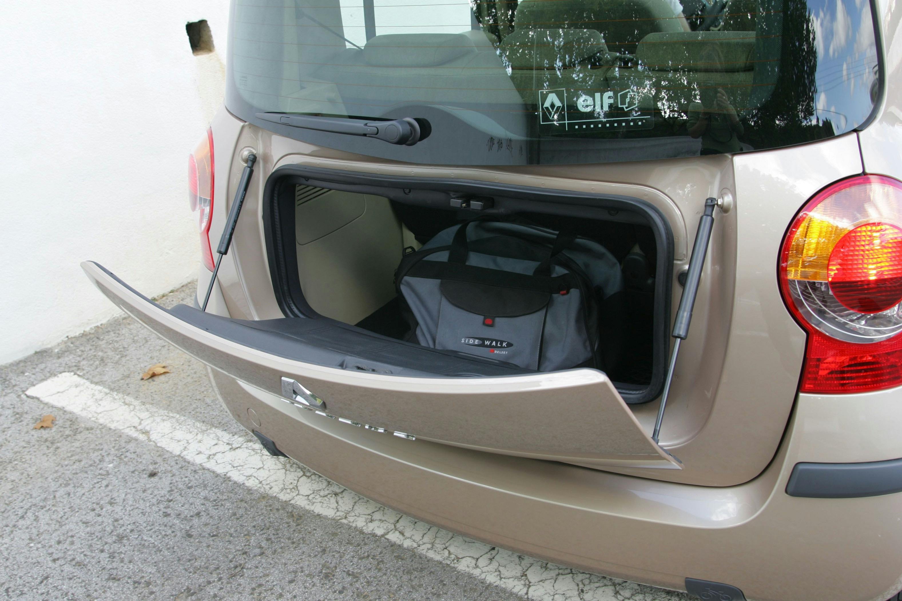 Ein goldfarbener Pkw mit geöffneter Heckklappe zeigt eine Tasche im Kofferraum. Das Fahrzeug steht auf einem Parkplatz.