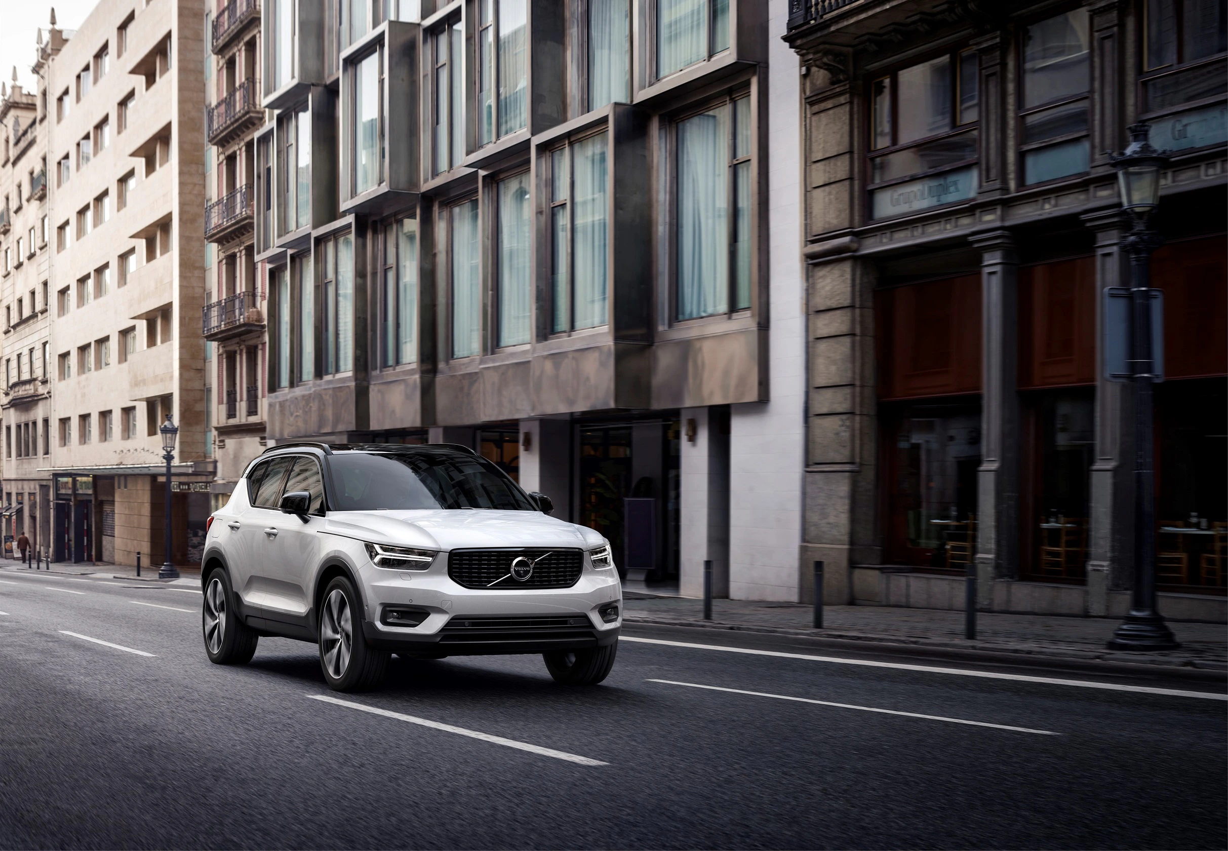 Ein weißer SUV fährt auf einer städtischen Straße mit modernen Gebäuden im Hintergrund. Es ist ein heller Tag.