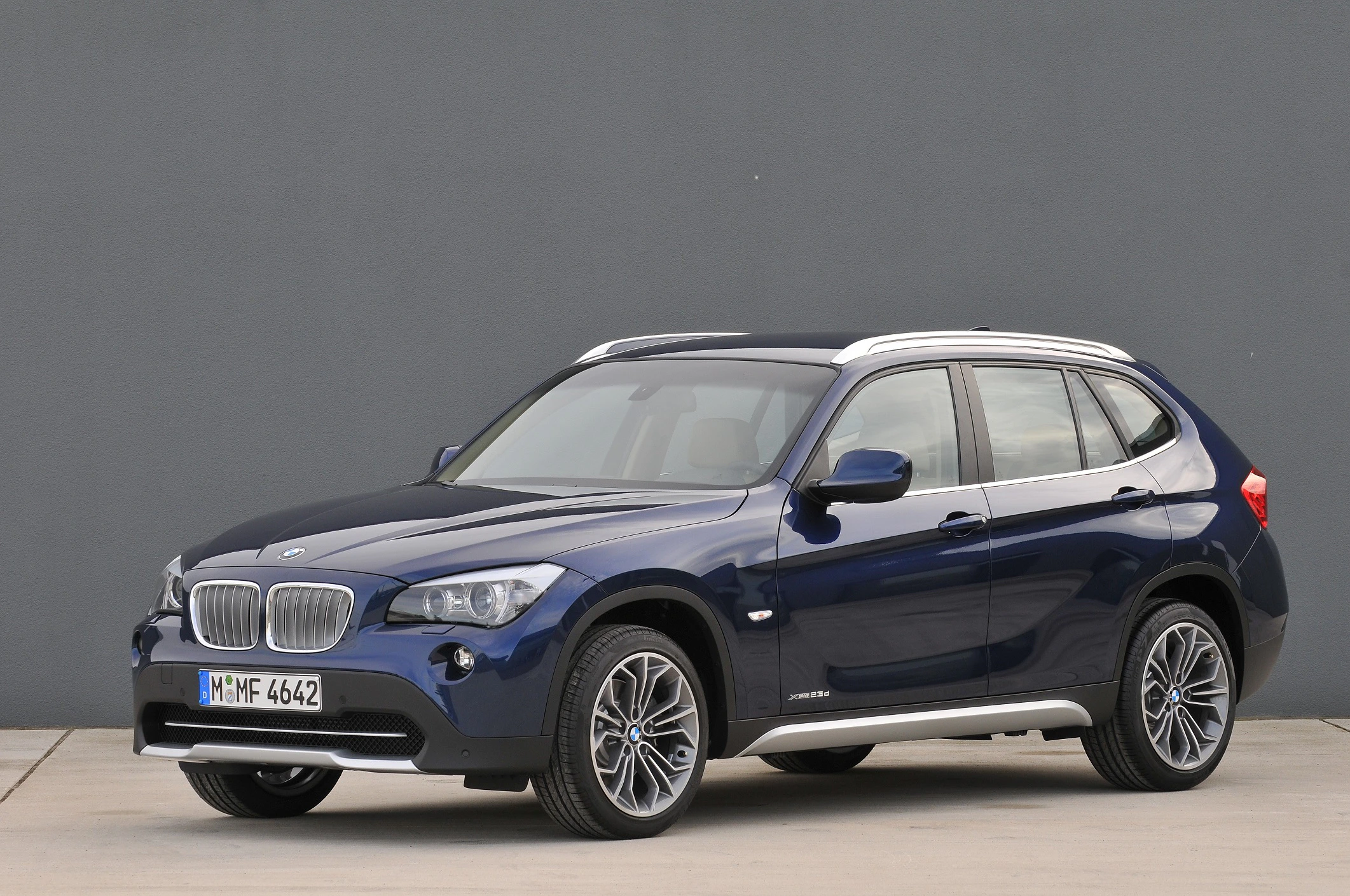 Dunkelblauer BMW X1 SUV steht auf grauem Boden vor einer grauen Wand, seitlicher Blick nach vorne links.