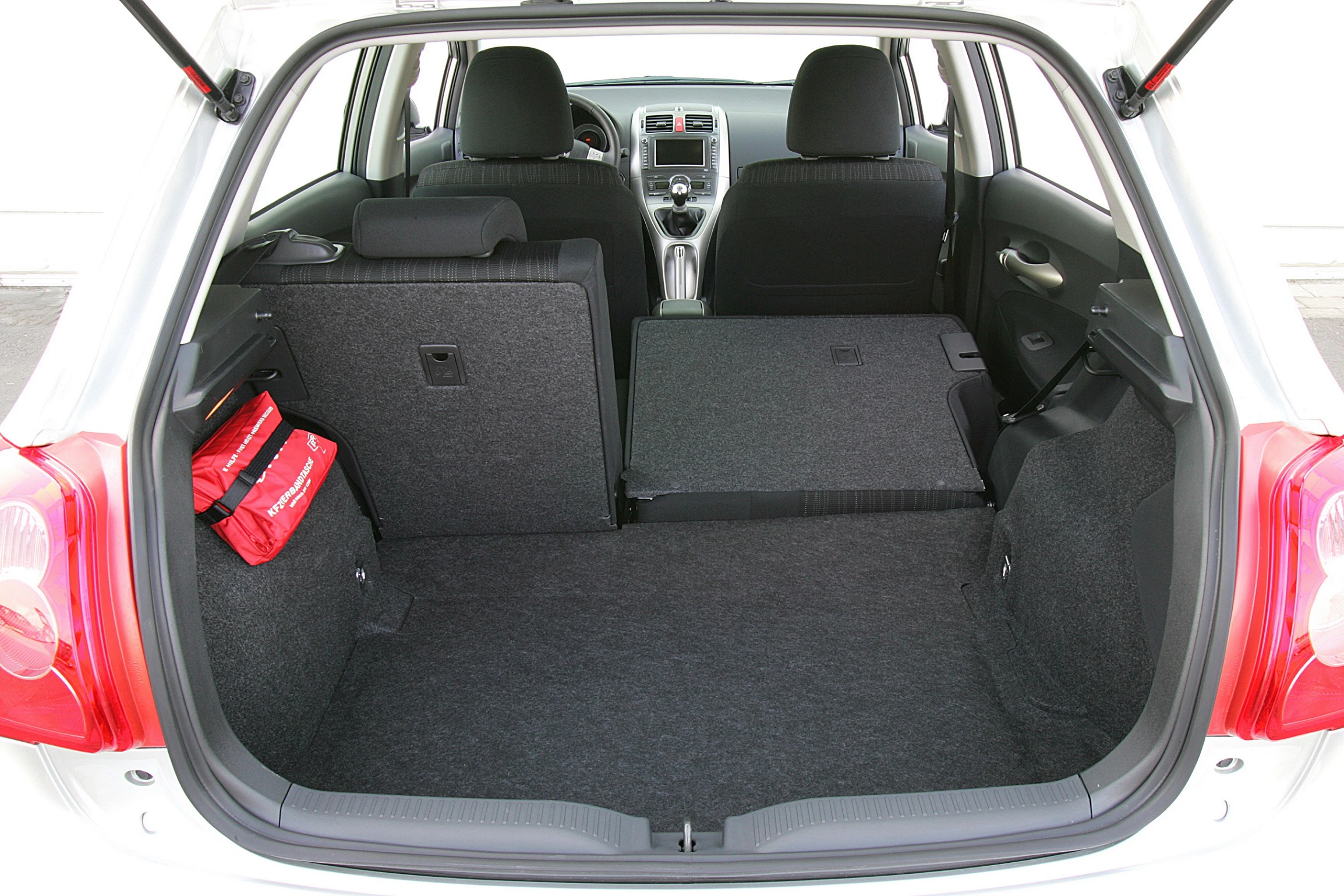 Kofferraum eines Autos mit umgeklappter Rückbank, zeigt viel Laderaum, schwarzen Teppichboden und einen roten Notfalltasche an der Seite.