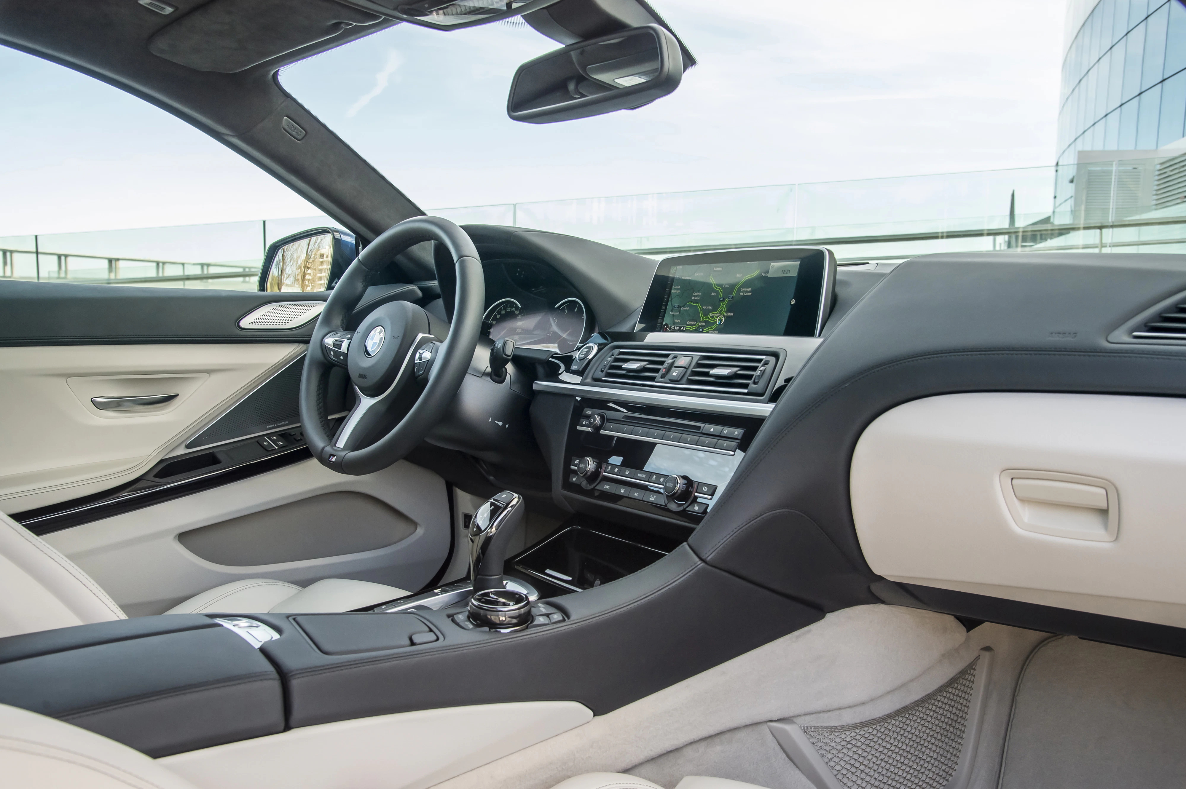 Innenraum eines modernen Autos mit Lederpolstern, zentralem Touchscreen, Automatikgetriebe und elegantem Lenkrad. Helle und dunkle Farbtöne.