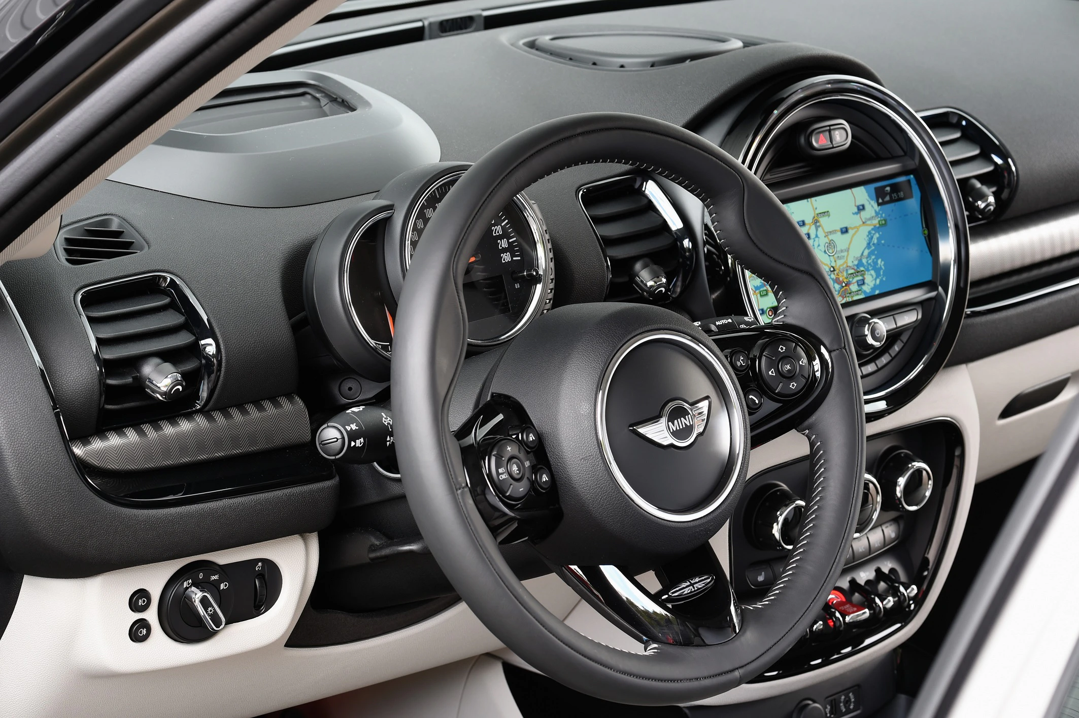 Innenraum eines Autos mit Lederlenkrad, Tachometer und Display mit Kartenansicht. Moderne Bedienelemente und Lüftungsdüsen sind sichtbar.