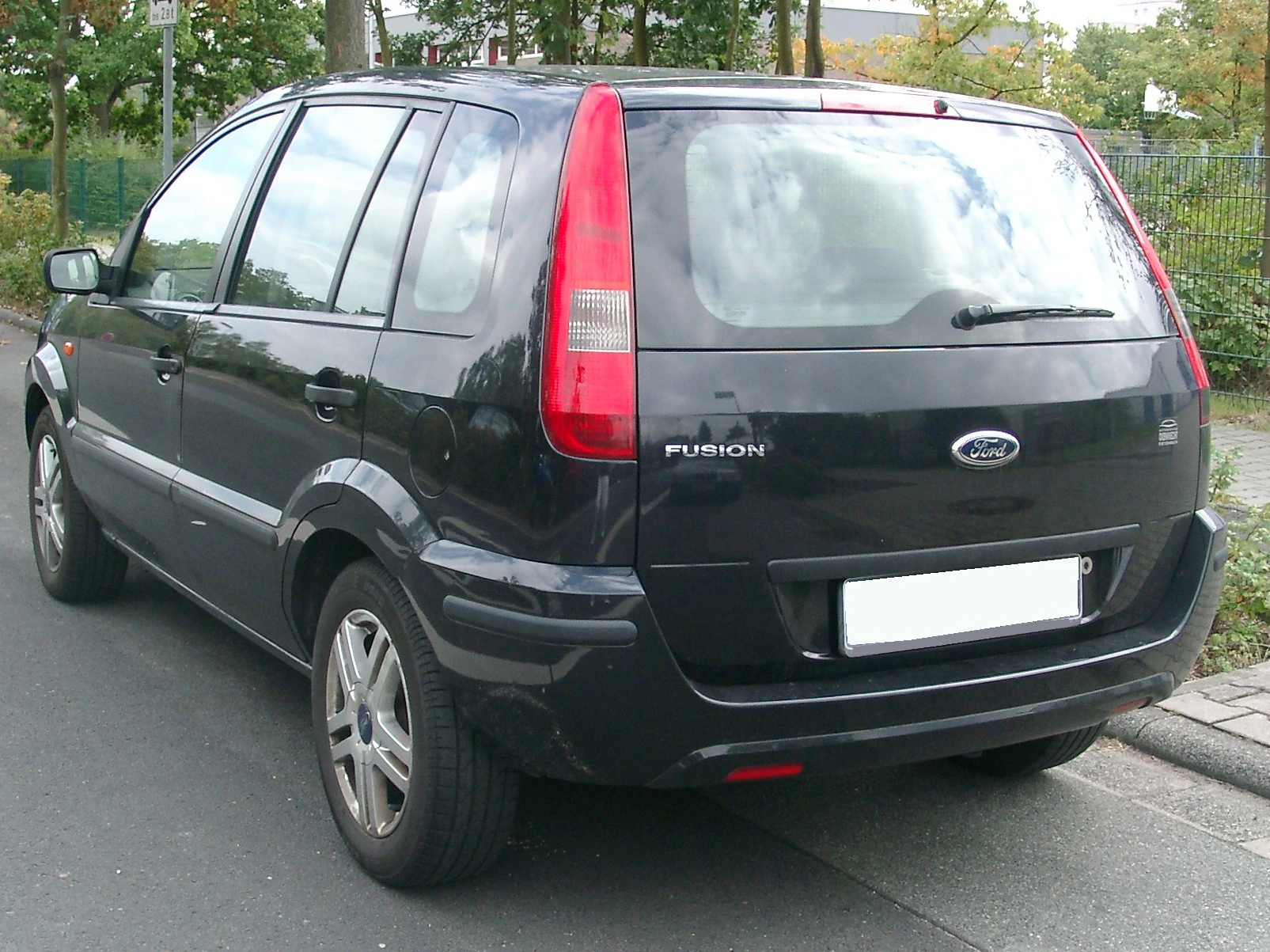Schwarzer Ford Fusion, geparkt auf einer Straße, Heckansicht. Reflektierende Rücklichter und silberne Felgen sichtbar.