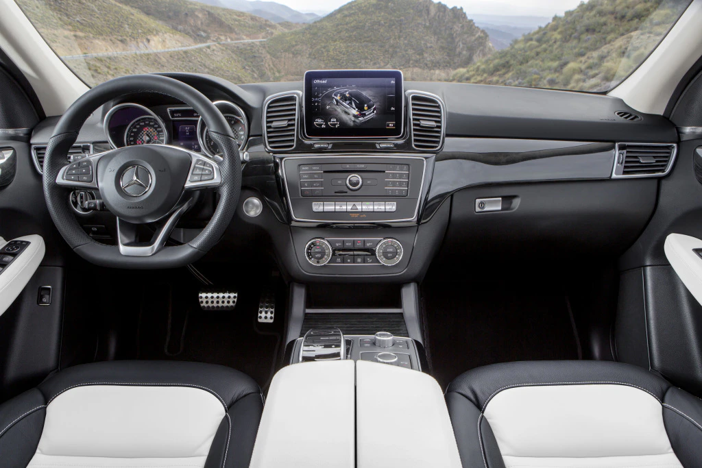 Innenansicht eines Mercedes-Benz mit modernem Armaturenbrett, Lenkrad und Display, umgeben von Berglandschaft.