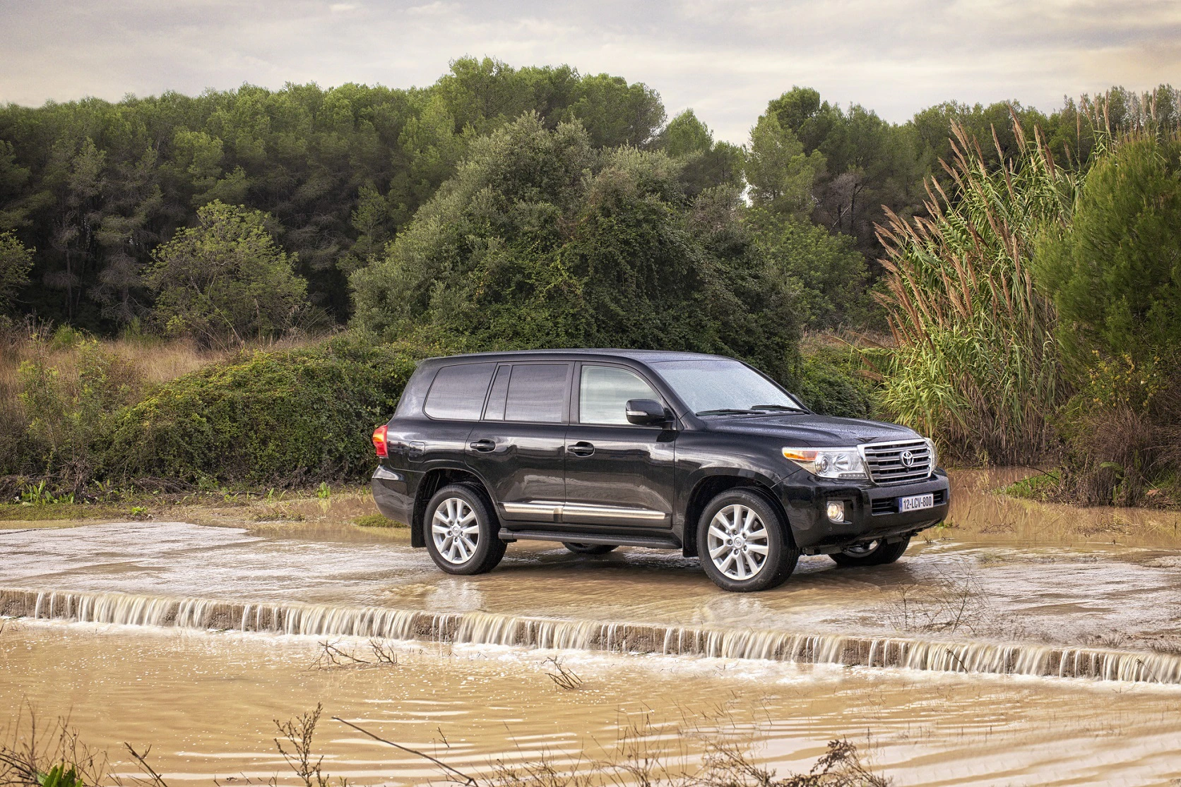 Ein schwarzer SUV fährt auf einer nassen Strecke mit fließendem Wasser und von Bäumen umgeben.