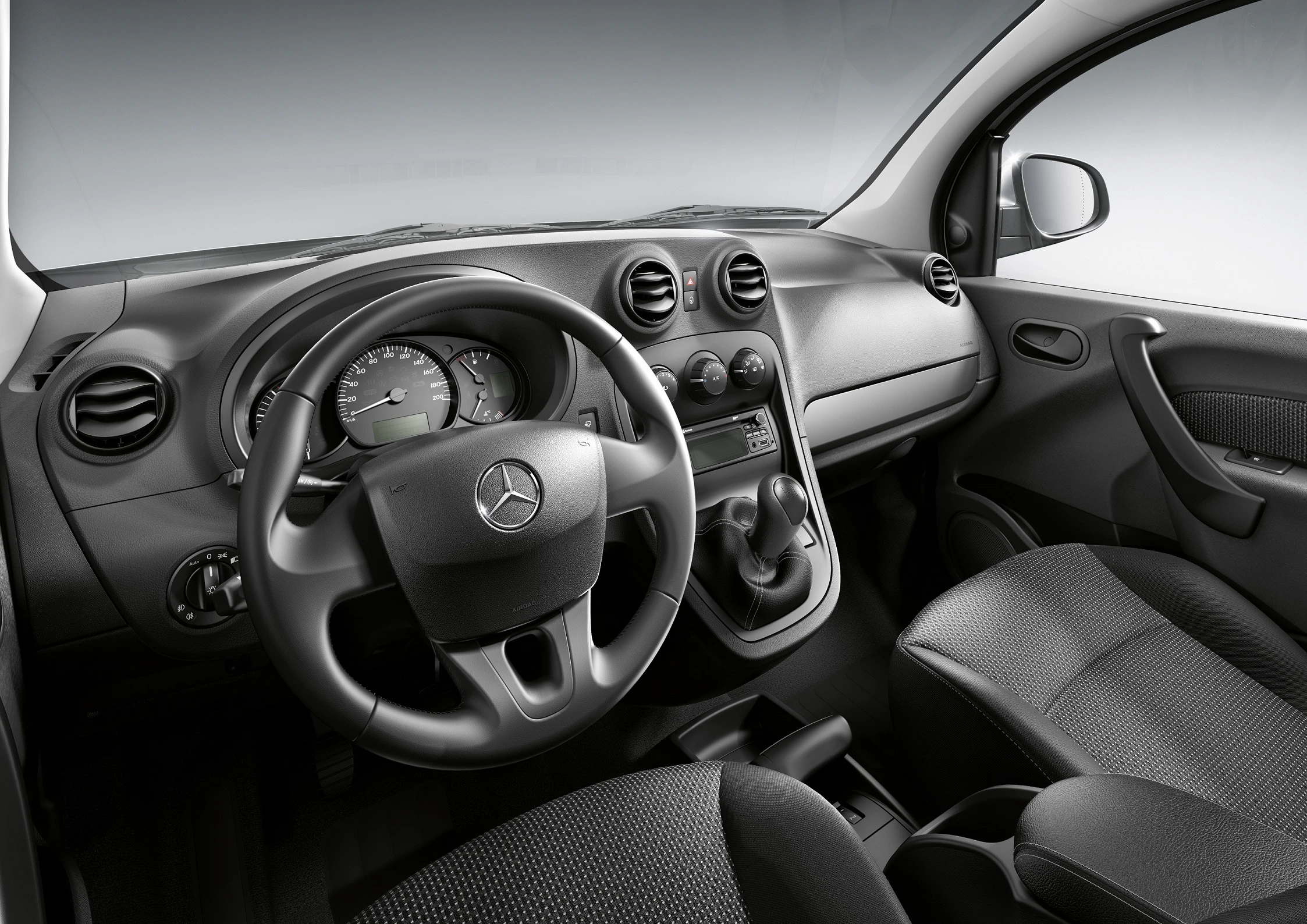 Innenraum eines Mercedes-Benz-Autos mit schwarzem Armaturenbrett, Lenkrad und Schalthebel. Die Sitze sind ebenfalls in dunklen Tönen gehalten.