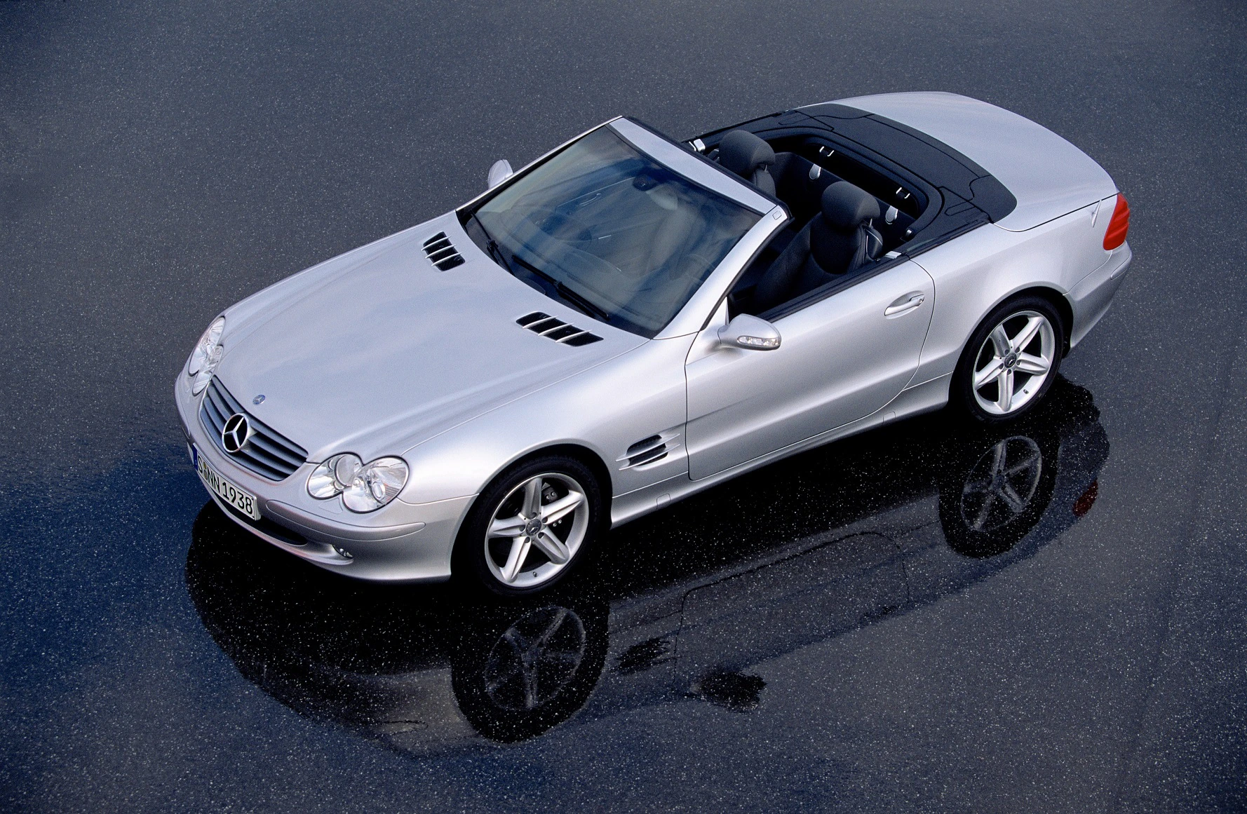 Silberner Mercedes-Benz SL 500 Cabriolet, Draufsicht, auf nasser Straße, mit geöffnetem Verdeck und glänzenden Karosseriedetails.