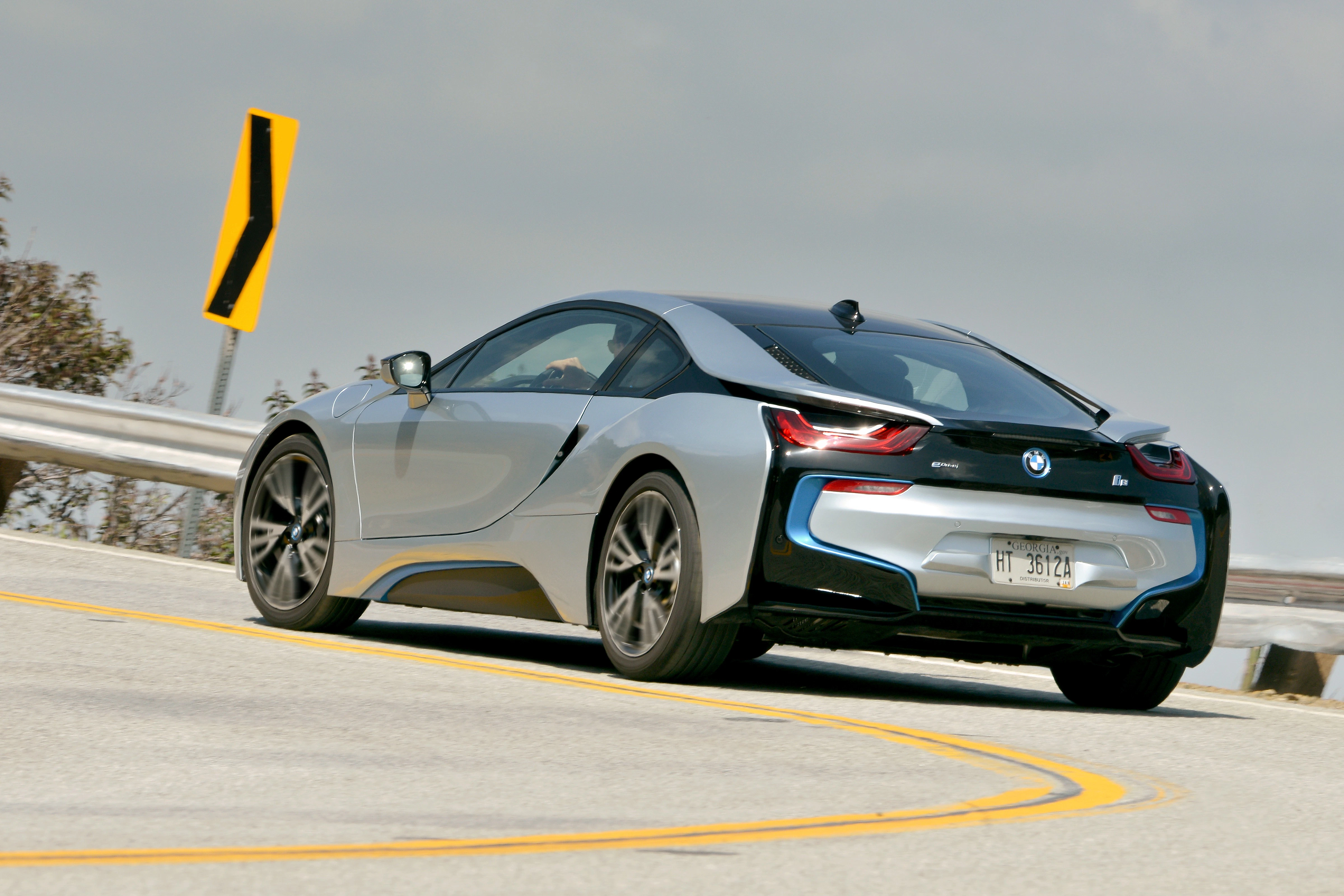 Silberner BMW i8 fährt auf einer kurvigen Landstraße. Dynamische Linien und moderner Sportwagendesign erkennbar.