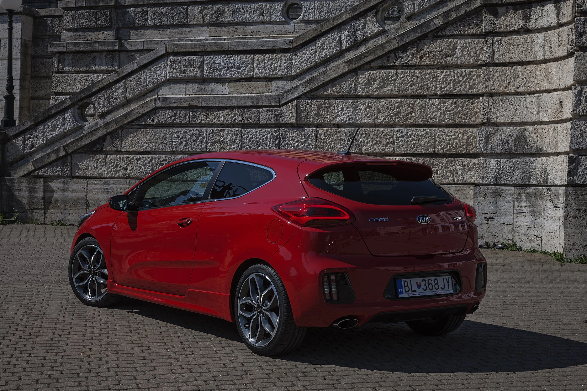Roter Sportwagen parkt vor einer historischen Steintreppe. Das Auto hat zwei Türen und auffällige Felgen.