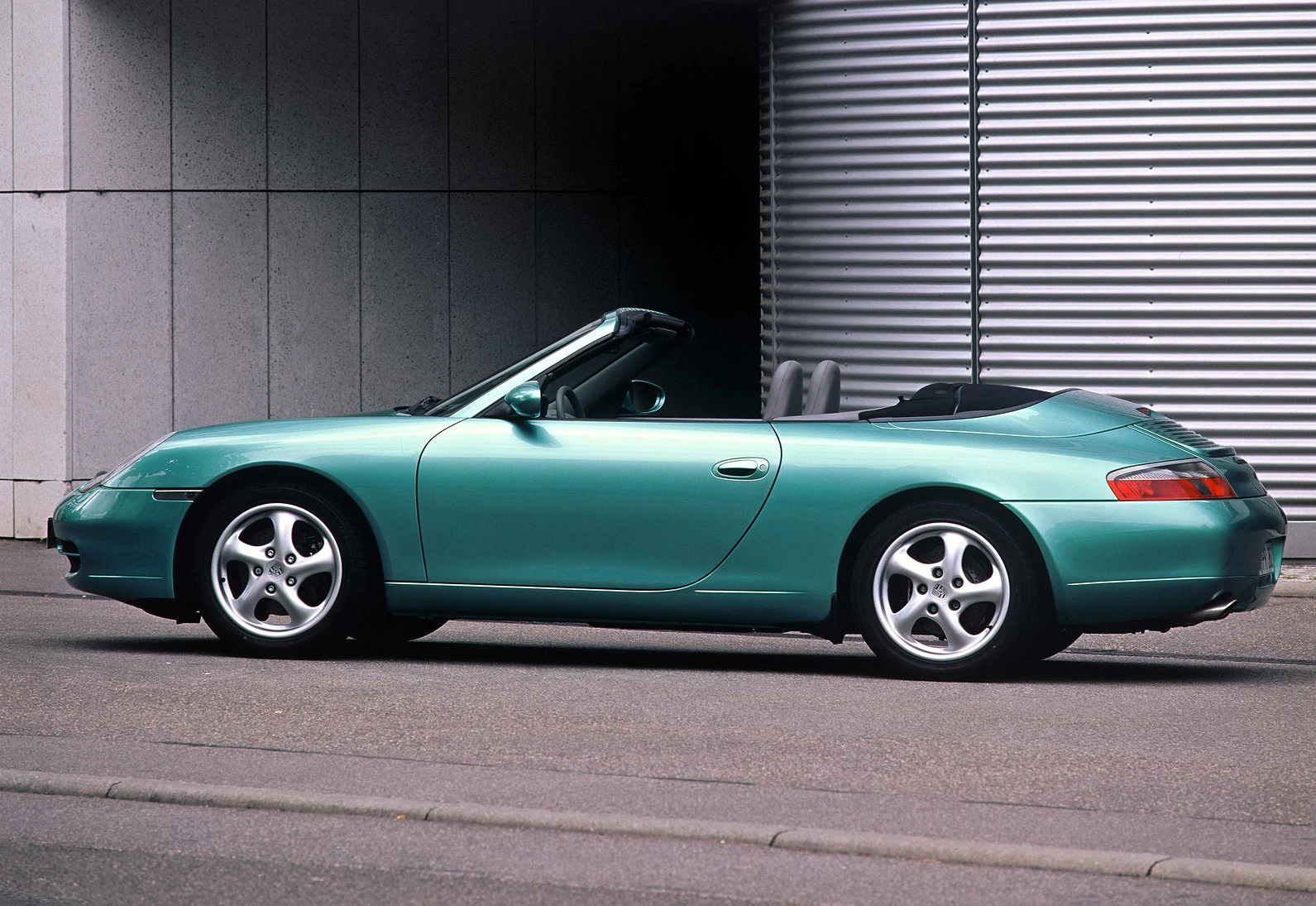 Grünes Cabrio-Sportauto parkt vor einem modernen Gebäude mit Metallverkleidung und Betonwand.