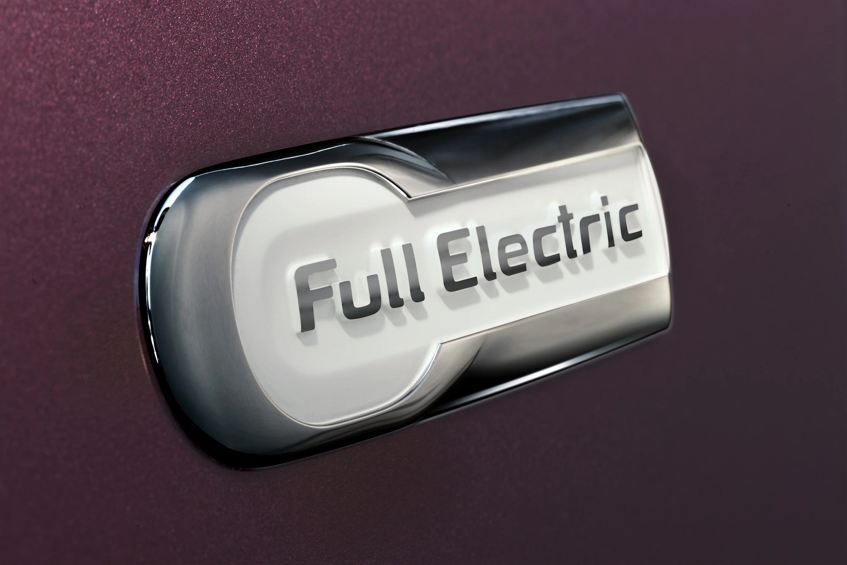 Nahaufnahme eines silbernen und weißen Emblems mit der Aufschrift "Full Electric" auf einer dunkelroten Oberfläche.