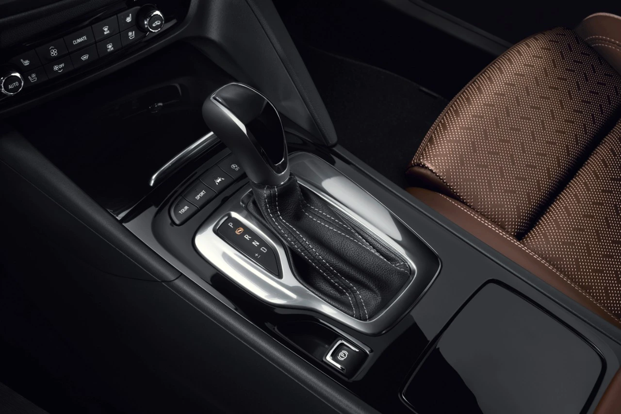 Nahaufnahme eines Automatikgetriebes in einem Auto, umgeben von schwarzem Interieur und braunem, gemustertem Sitzbezug.