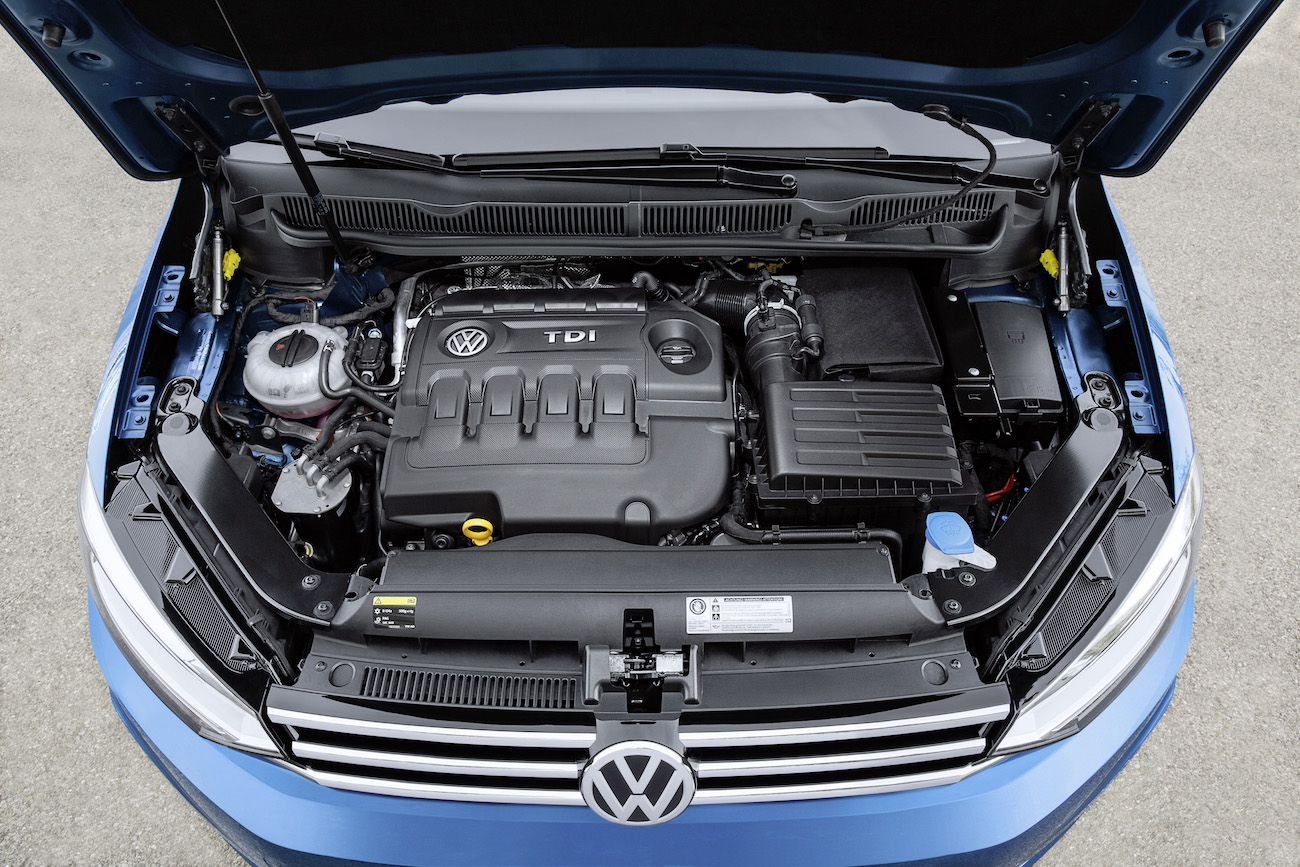 Motorraum eines blauen Volkswagen mit TDI-Motor. Motorabdeckung, Luftfilter und andere Komponenten sind erkennbar.