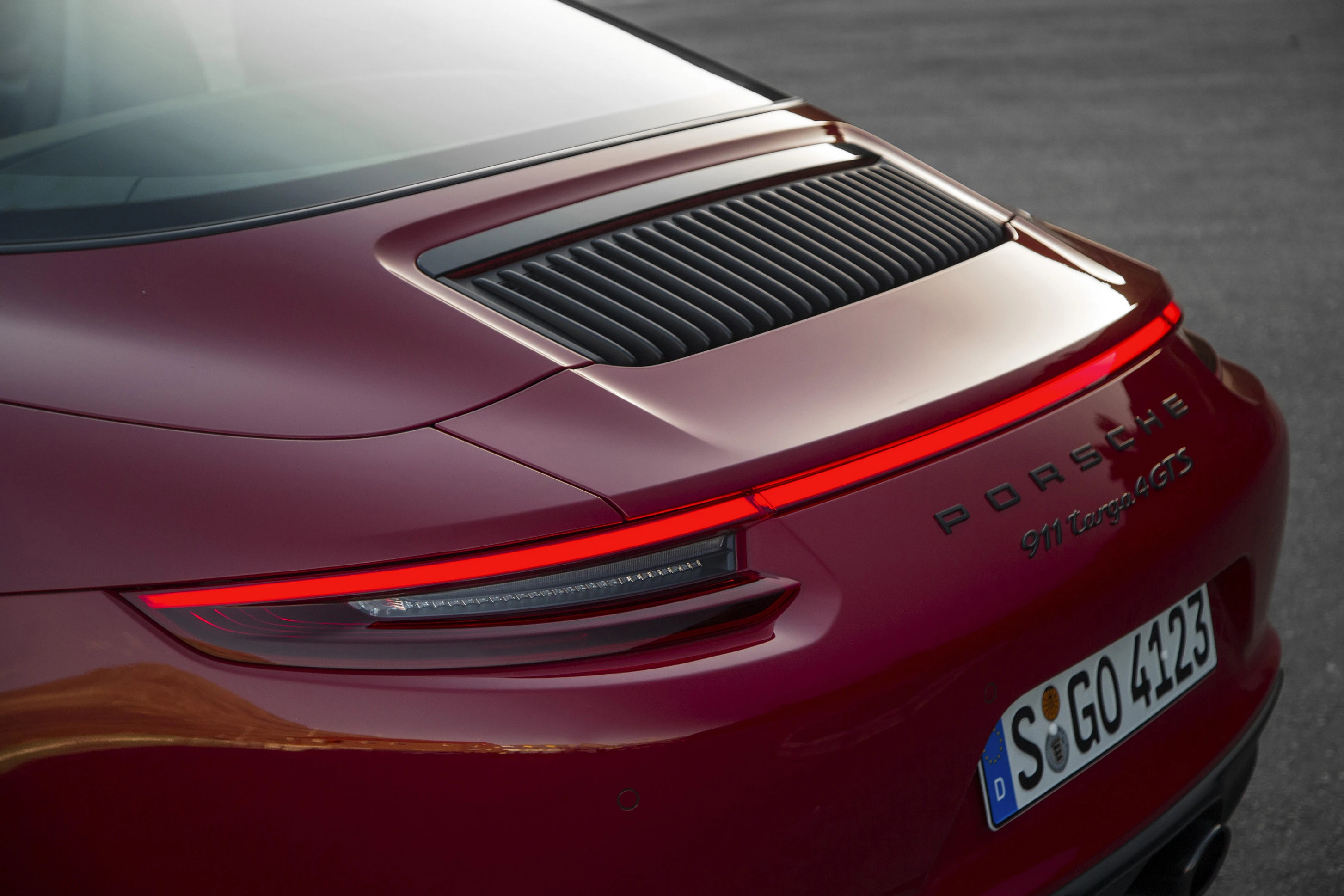 Heckansicht eines roten Porsche 911 Carrera S. Gut sichtbare Rückleuchte, Lüftungsschlitze und Nummernschild auf grauem Asphalt.