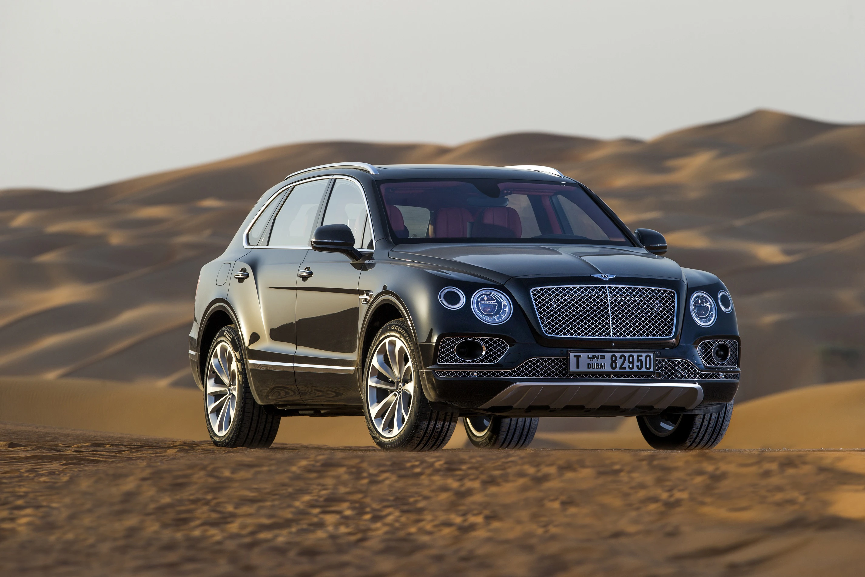 Schwarzer SUV parkt in einer Sandlandschaft mit Dünen im Hintergrund. Fahrzeug mit luxuriösem Design und Nummernschild aus Dubai.