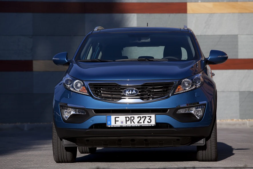 Blauer Kia SUV frontal fotografiert vor einer Wand mit horizontalen Streifen in Blau- und Brauntönen.