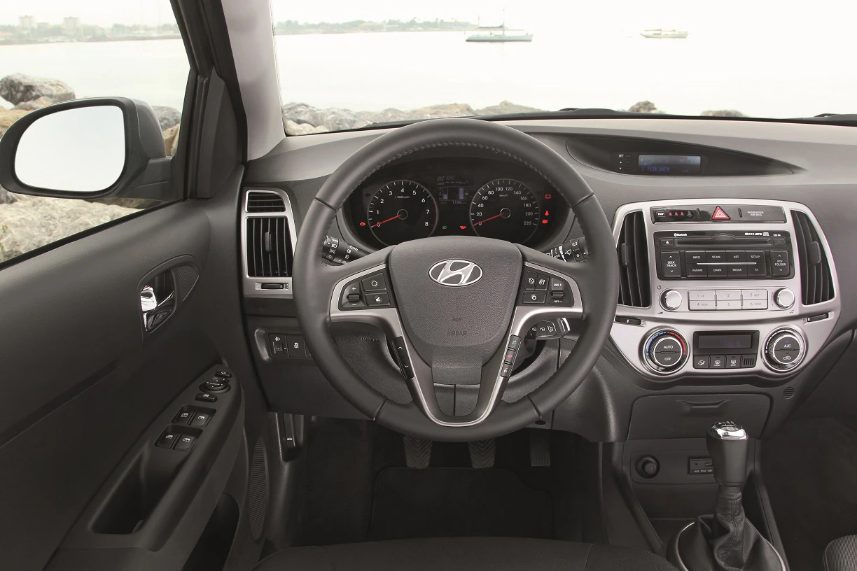 Innenraum eines Autos mit Hyundai-Logo auf dem Lenkrad, Armaturenbrett mit Anzeigen und Audiosystem, Blick auf Meer durch Fenster.