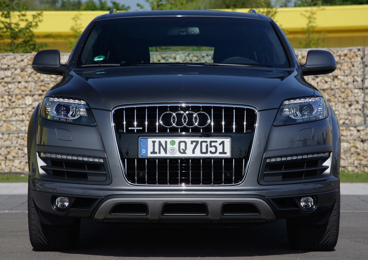 Frontansicht eines grauen Audi Q7, geparkt auf einem Parkplatz, mit Fokus auf Kühlergrill und Scheinwerfer.