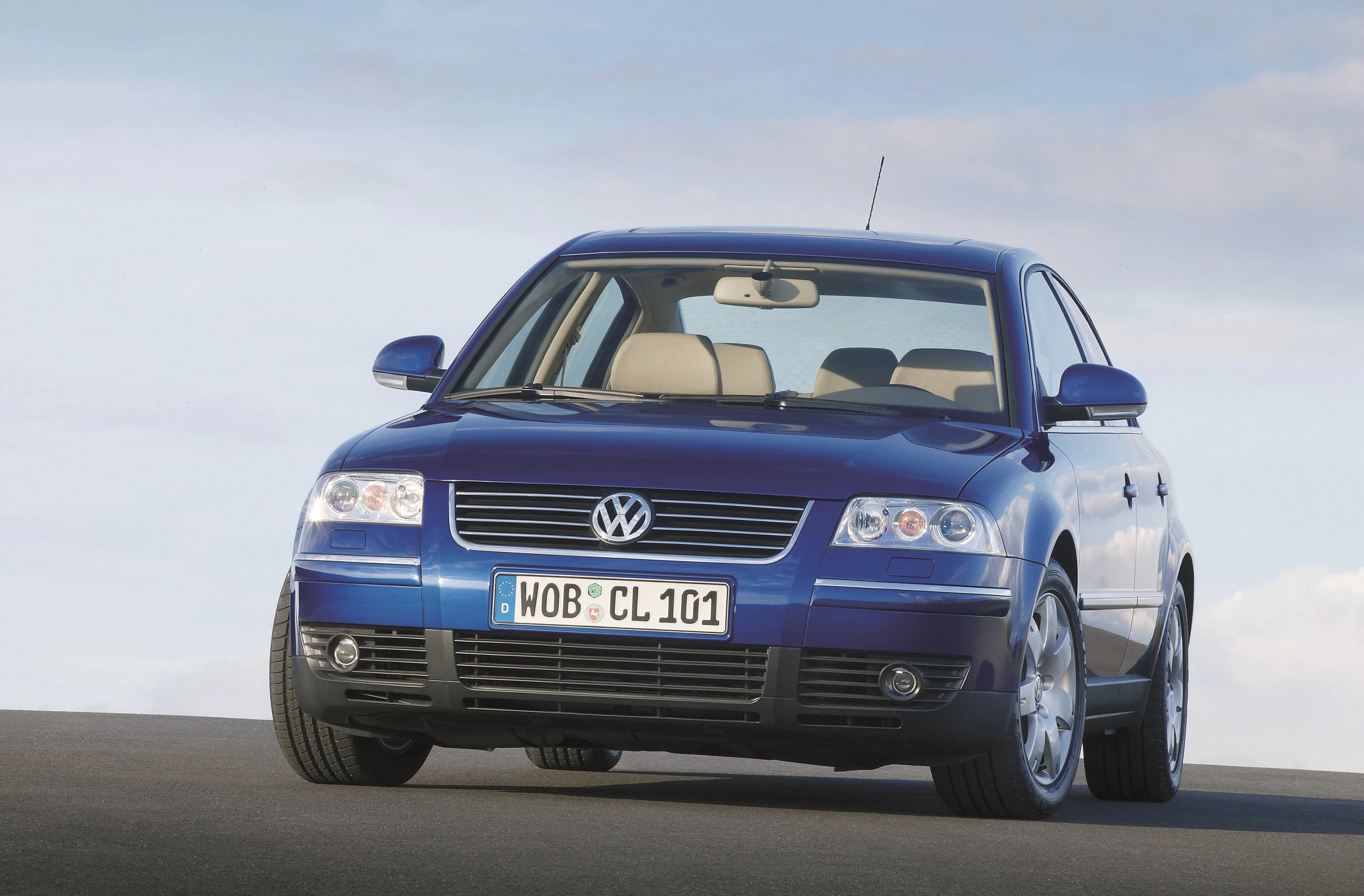 Blauer Volkswagen Passat auf einer Straße, fotografiert vor einem bewölkten Himmel. Frontansicht mit sichtbarem VW-Logo und Kennzeichen.