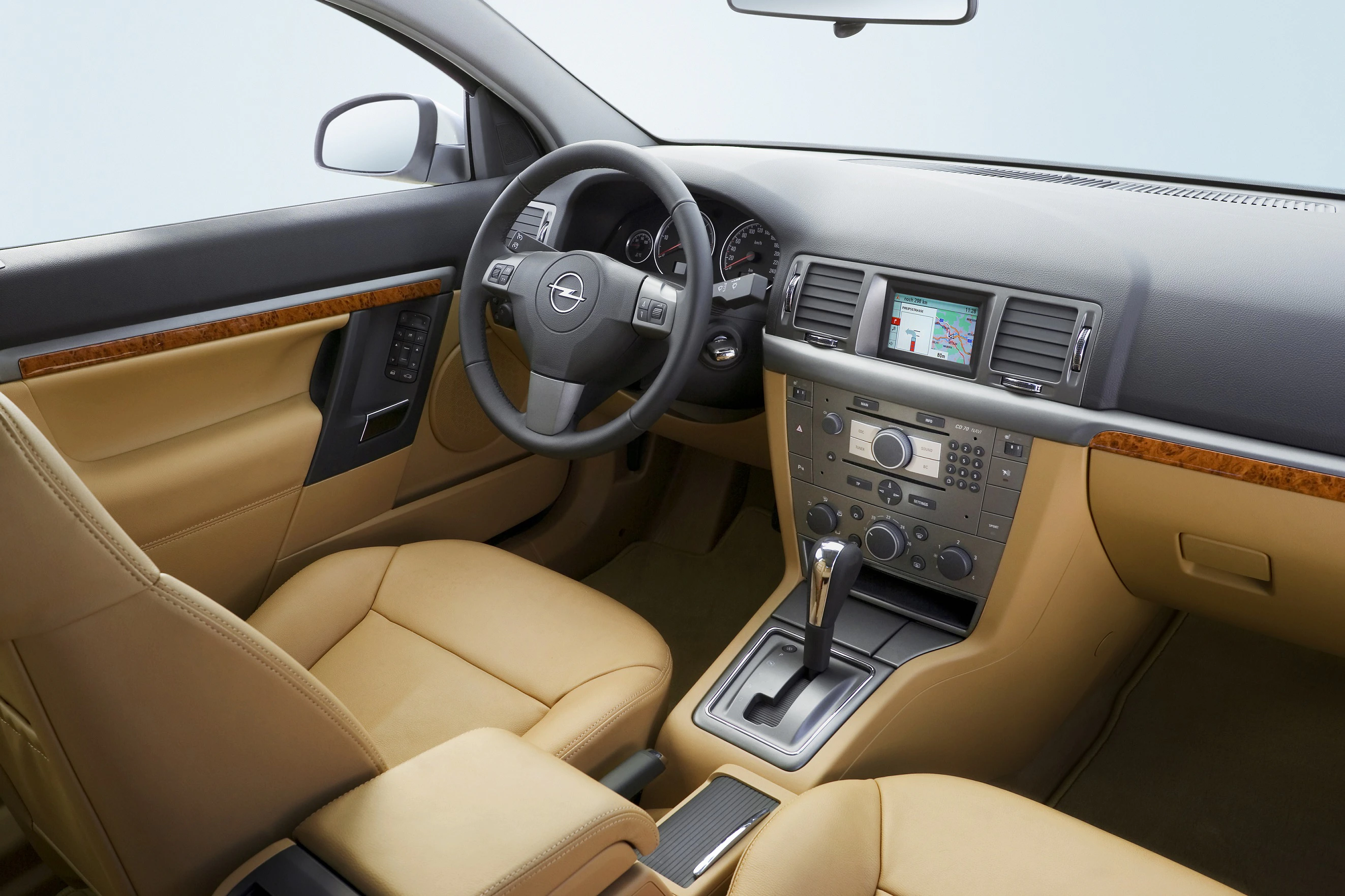 Innenraum eines Autos mit beigen Ledersitzen, schwarzem Armaturenbrett, integriertem Navigationssystem und Automatikgetriebe.