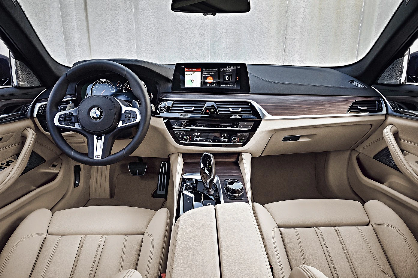 Innenraum eines BMW mit beigem Leder, modernem Armaturenbrett, Touchscreen, Multifunktionslenkrad und digitalen Anzeigeinstrumenten.