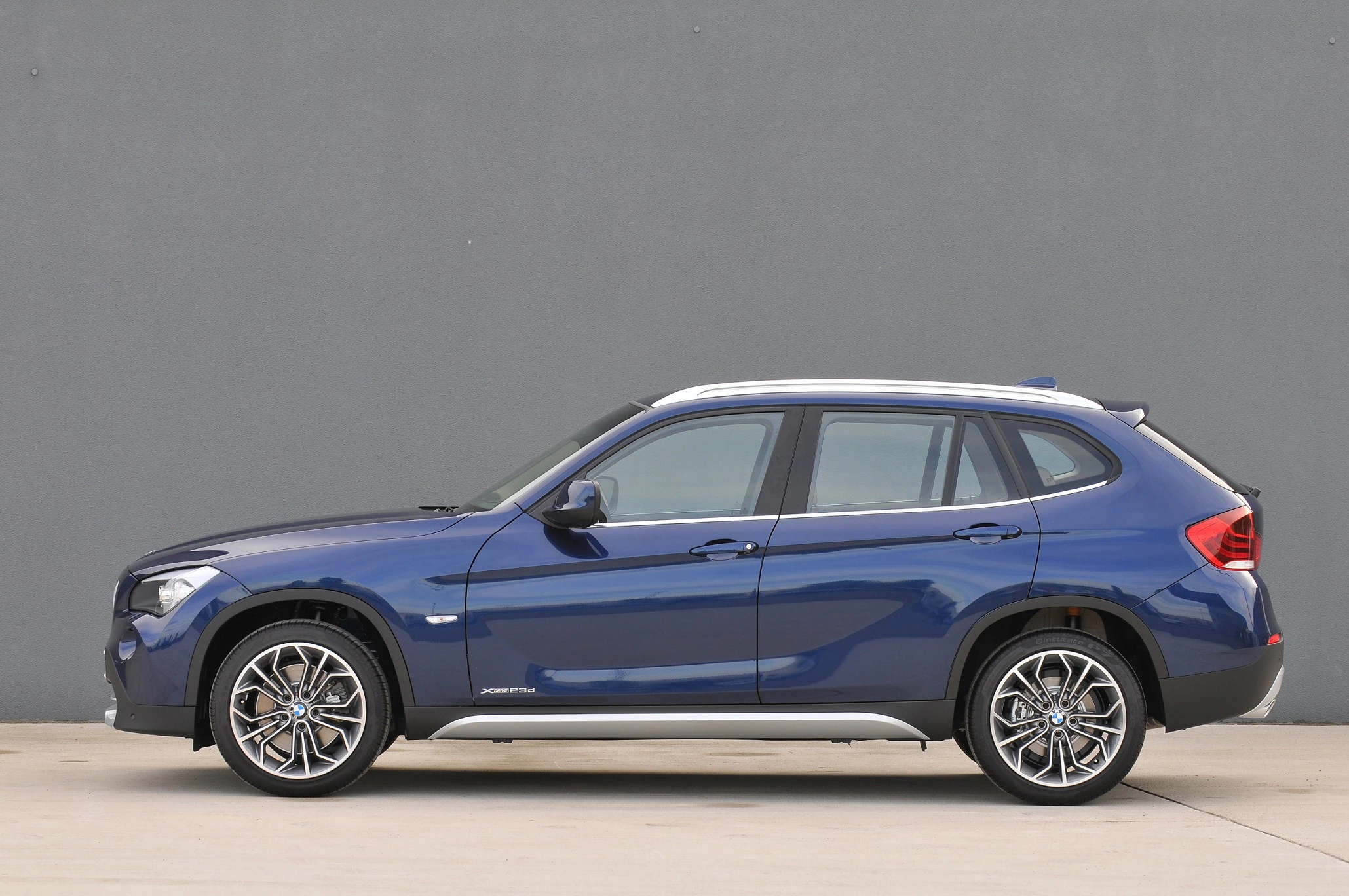 Blauer SUV vor grauem Hintergrund, Seitenansicht. Vier Türen und silberne Felgen, modernes Design. Fahrzeug steht auf hellem Boden.