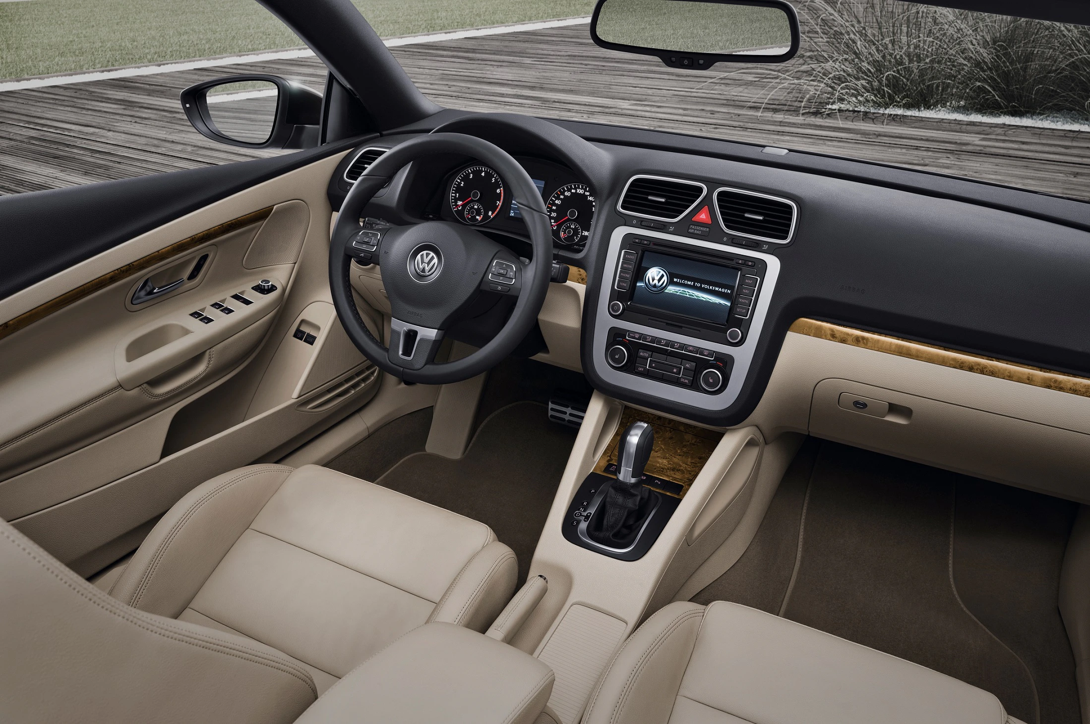 Innenraum eines Autos mit beigen Ledersitzen, schwarzem Armaturenbrett, Lenkrad mit VW-Logo und modernem Infotainment-Bildschirm.