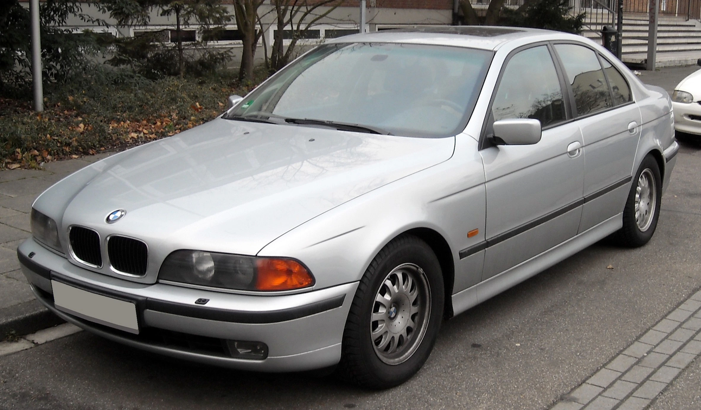 Silberner BMW E39 Limousine, geparkt auf einer Straße. Vorderseite und rechte Seite des Fahrzeugs sind sichtbar.