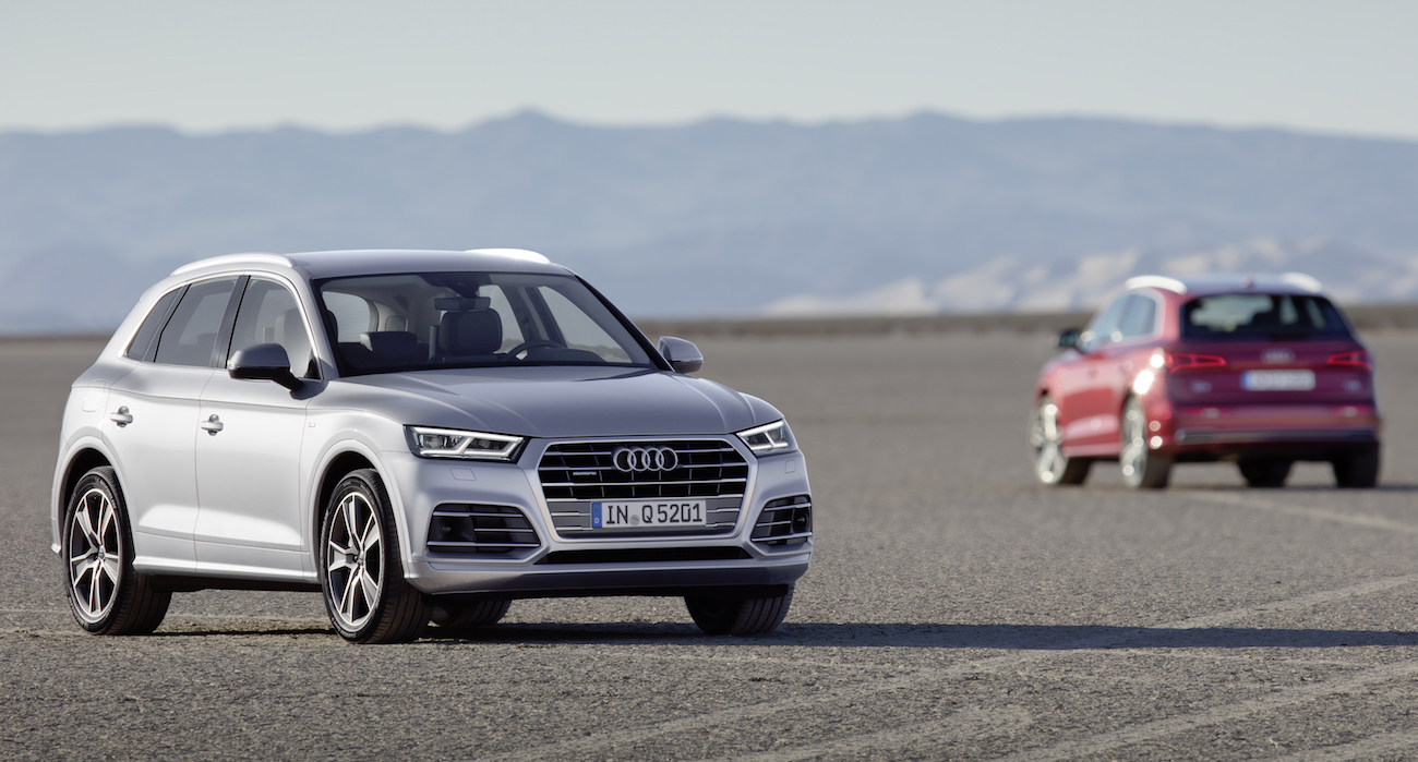 Zwei Audi-SUVs fahren über eine trockene, weite Landschaft. Im Vordergrund ein silberner SUV, im Hintergrund ein roter SUV.