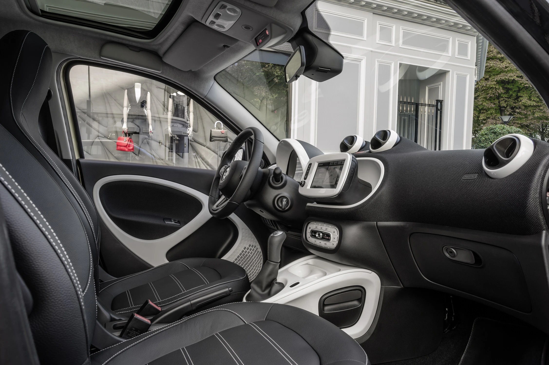 Innenraum eines modernen Kleinwagens mit schwarzer Lederpolsterung, Lenkrad, und Touchscreen-Display, durch Glasfenster Tageslicht.