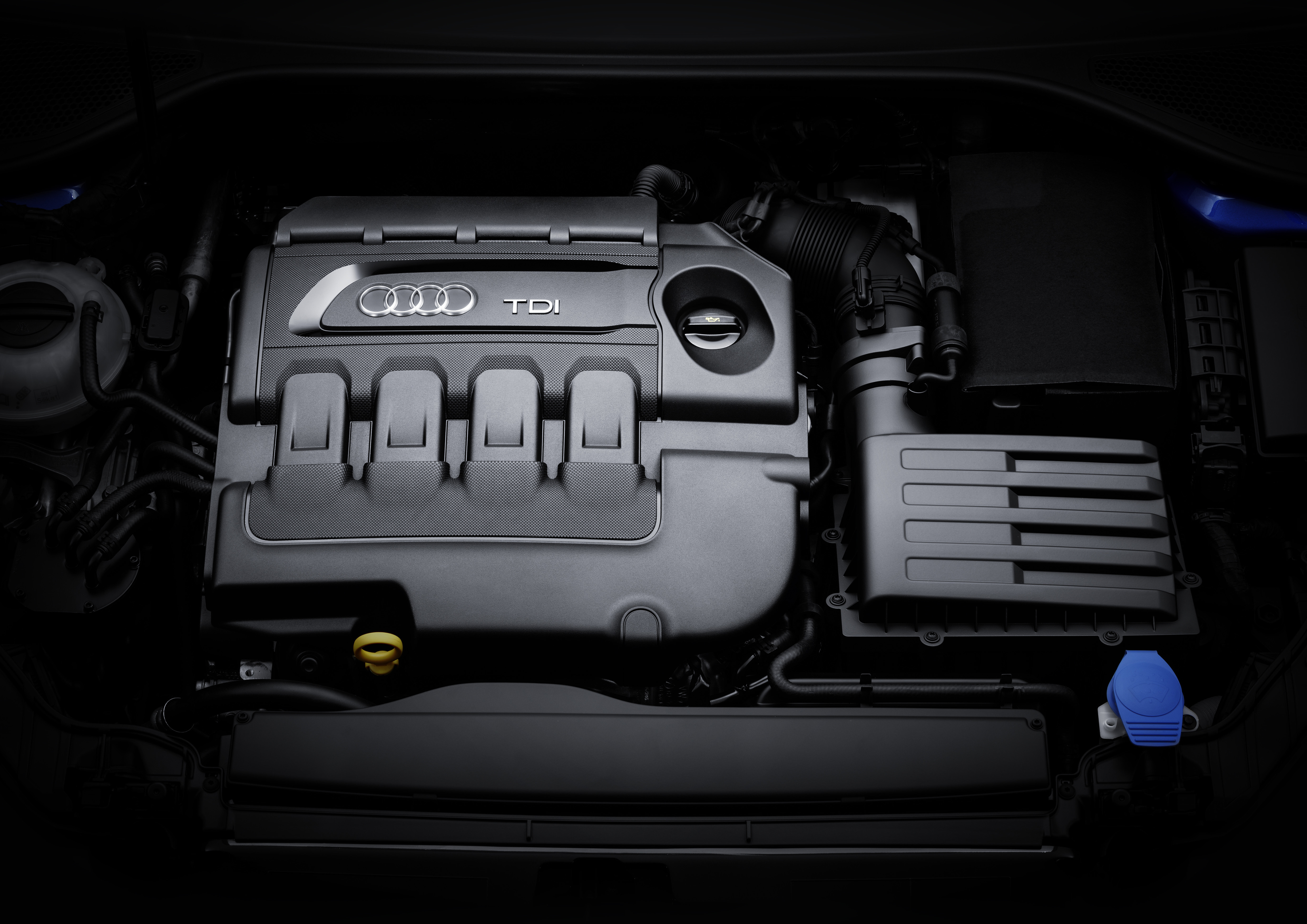 Motorraum mit Audi TDI-Motor, sichtbarem Öleinfüllstutzen und Luftfiltergehäuse, in schwarzer Umgebung.