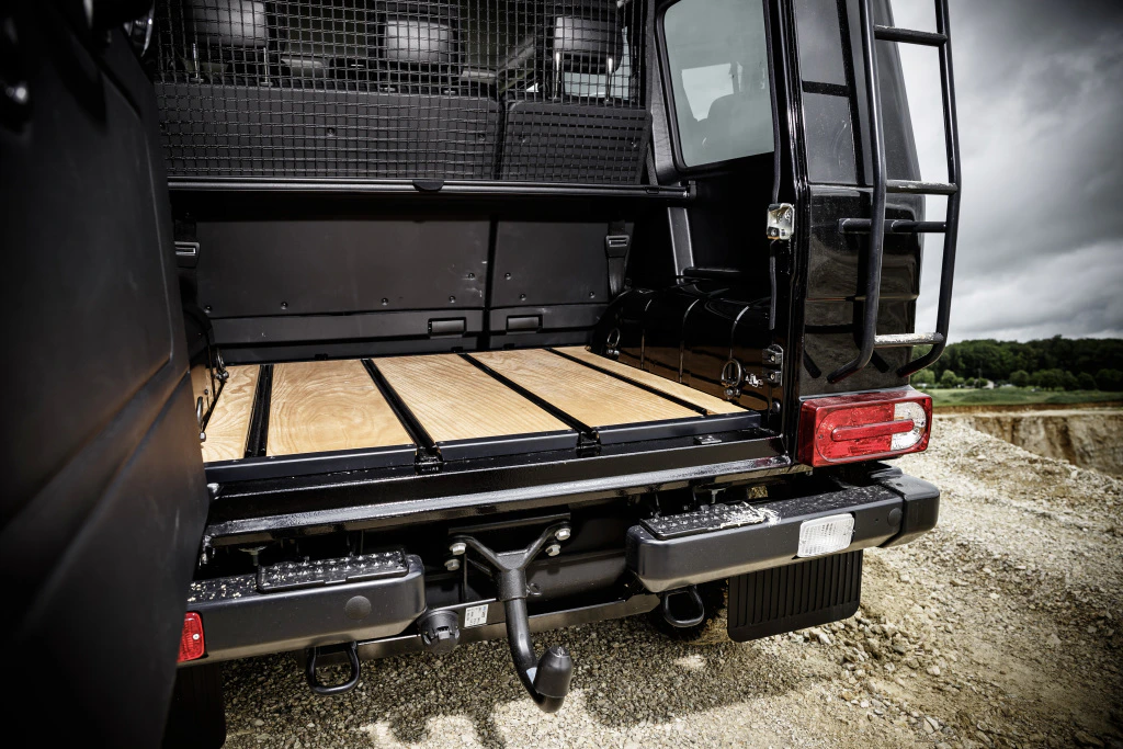 Schwarzer Geländewagen mit geöffnetem Kofferraum. Holzboden im Laderaum, Gelände im Hintergrund.