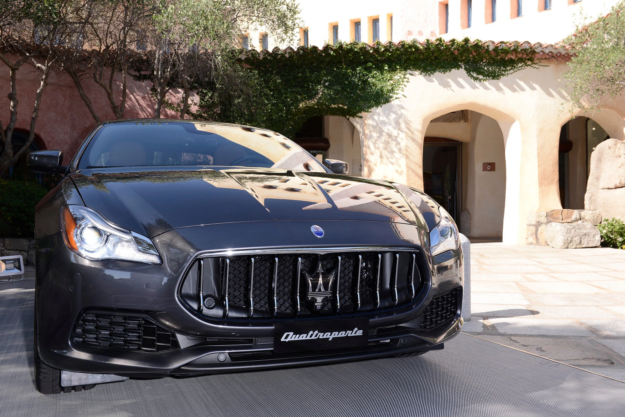 Luxuriöser, schwarzer Maserati Quattroporte steht vor mediterranem Gebäude mit Rundbögen und Bäumen im Hintergrund.